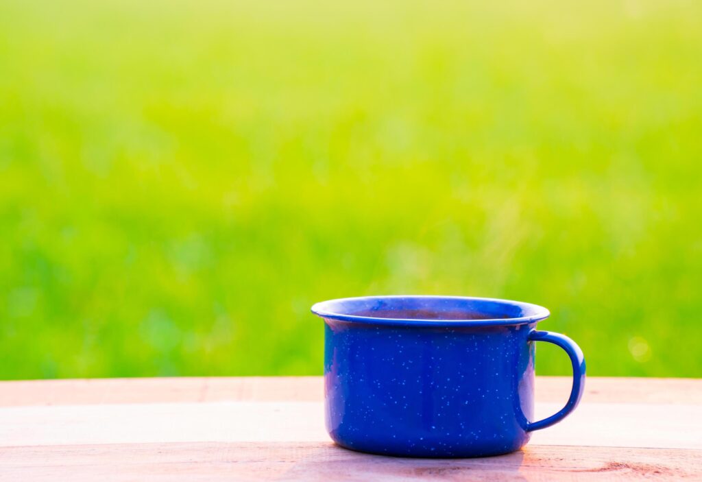 Kettle, blue enamel, and coffee mugs On an old wooden floor, Blurred background of rice fields at sunrise. Stock Free