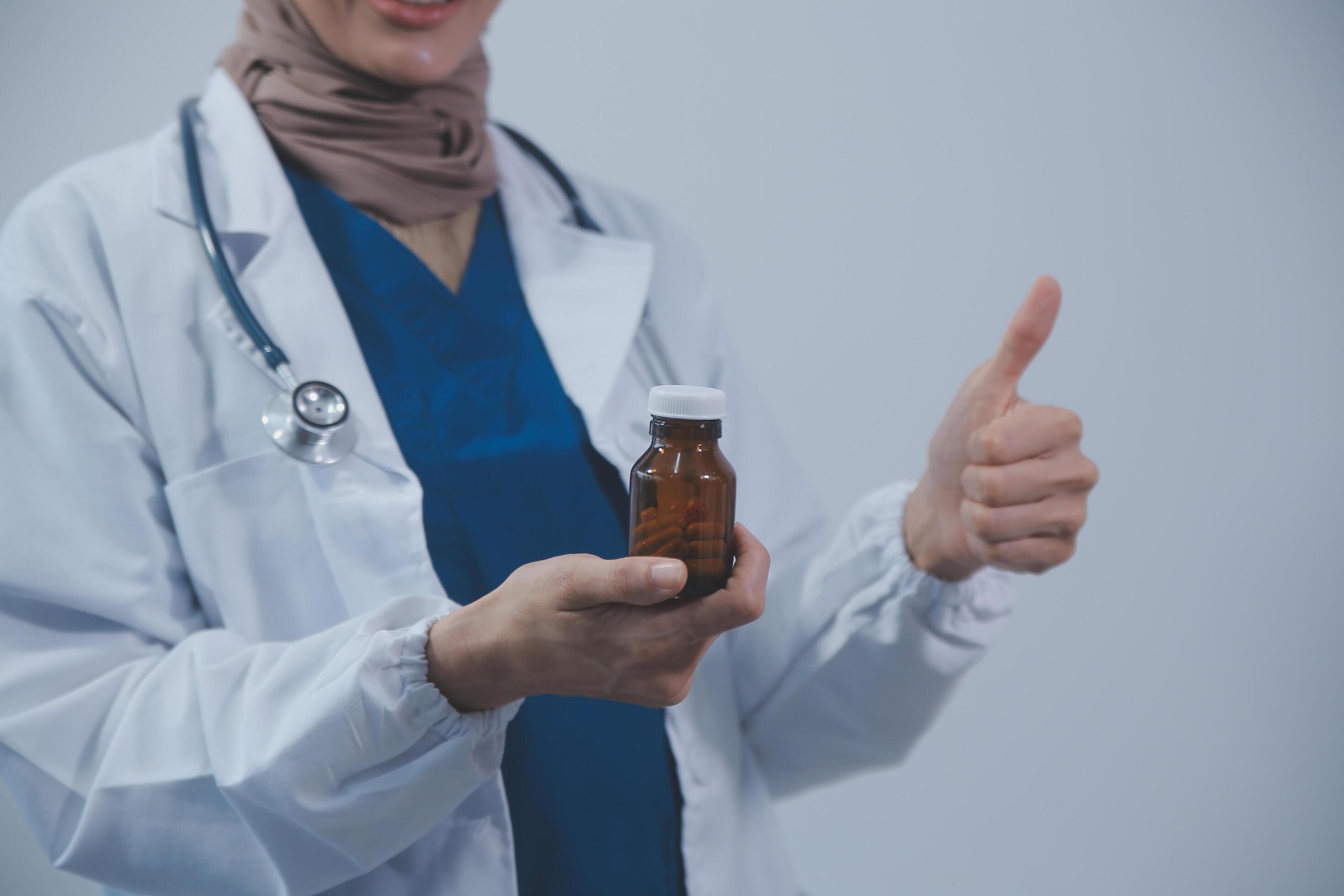 Southeast Asian medical doctor holding a bottle of pills, smiling isolated white background Stock Free