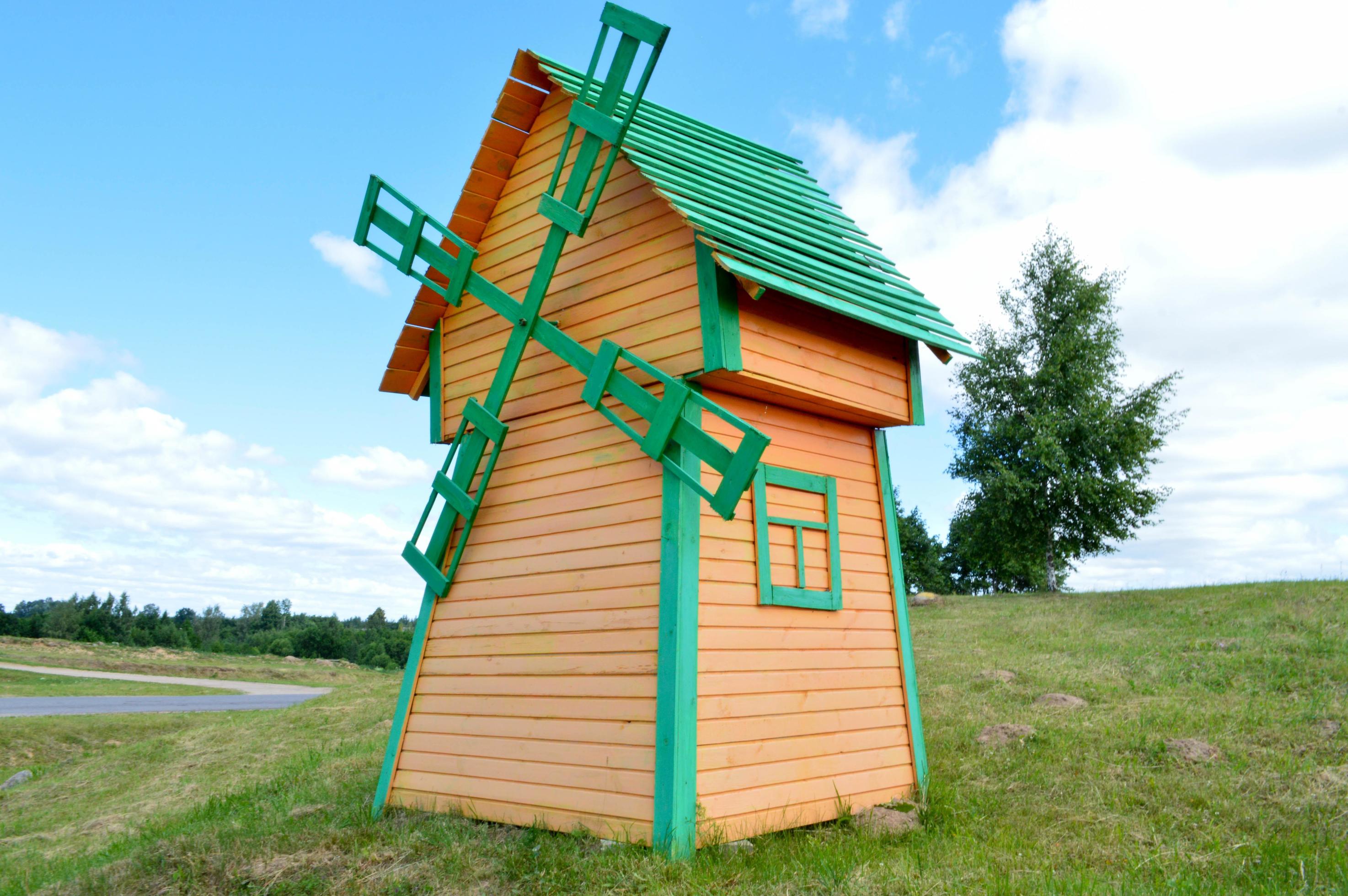 A beautiful wooden mill is a rustic natural windmill made of boards of yellow and green logs against a blue sky with clouds Stock Free