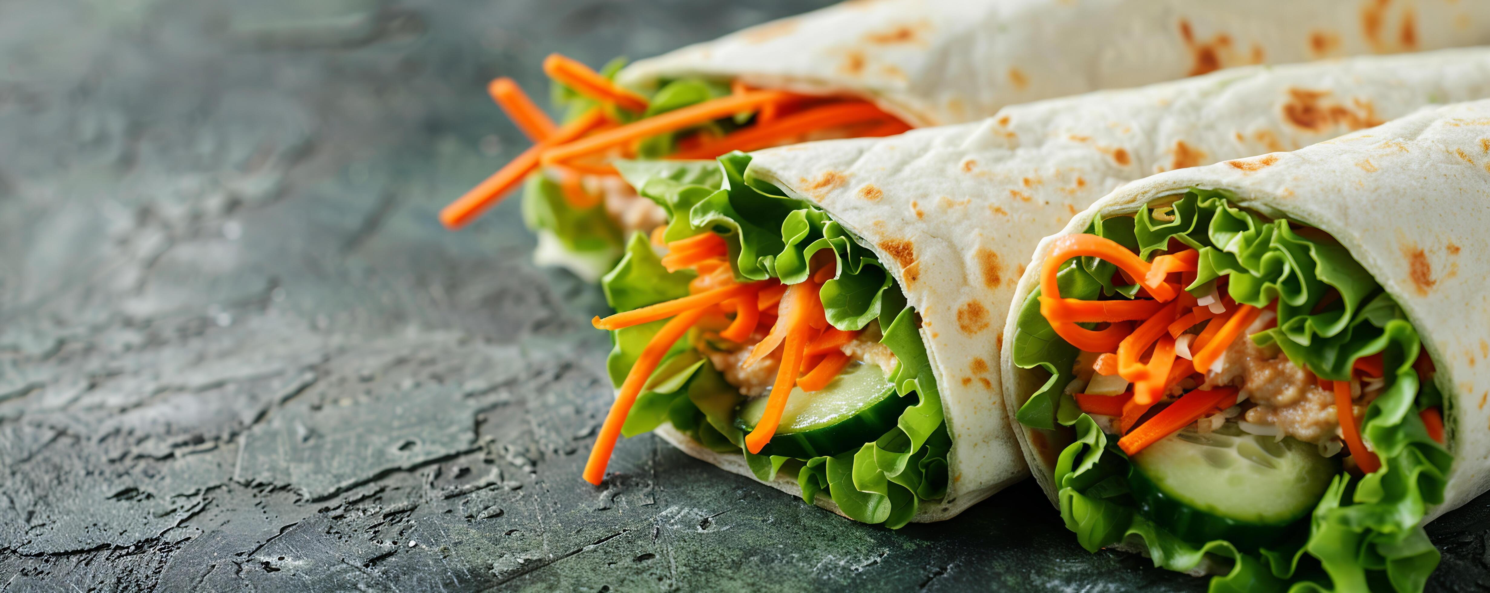 Colorful veggie wraps with hummus, shredded carrots, cucumbers, and lettuce. Stock Free