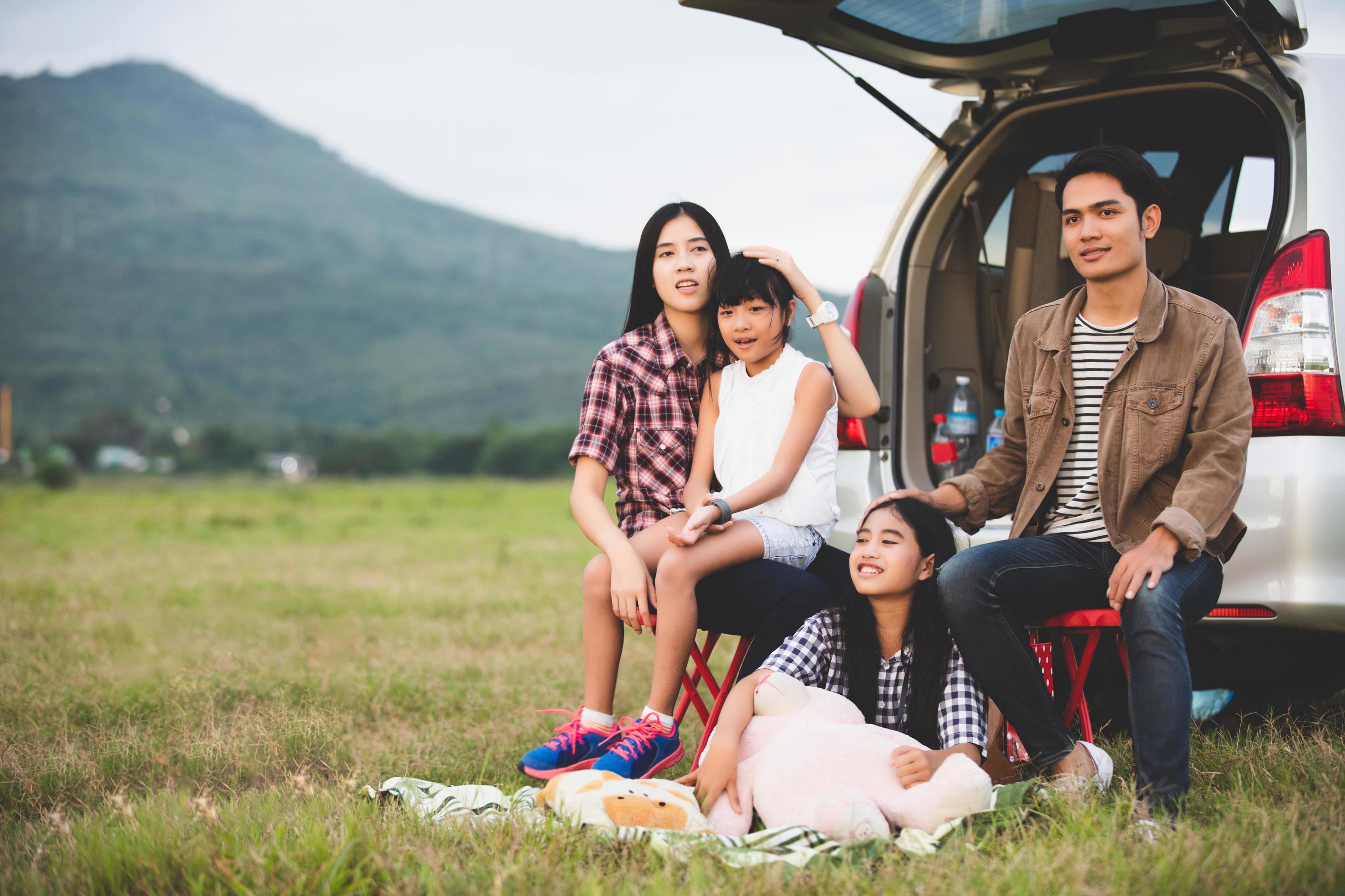 Happy little girl with asian family sitting in the car for enjoying road trip and summer vacation in camper van Stock Free