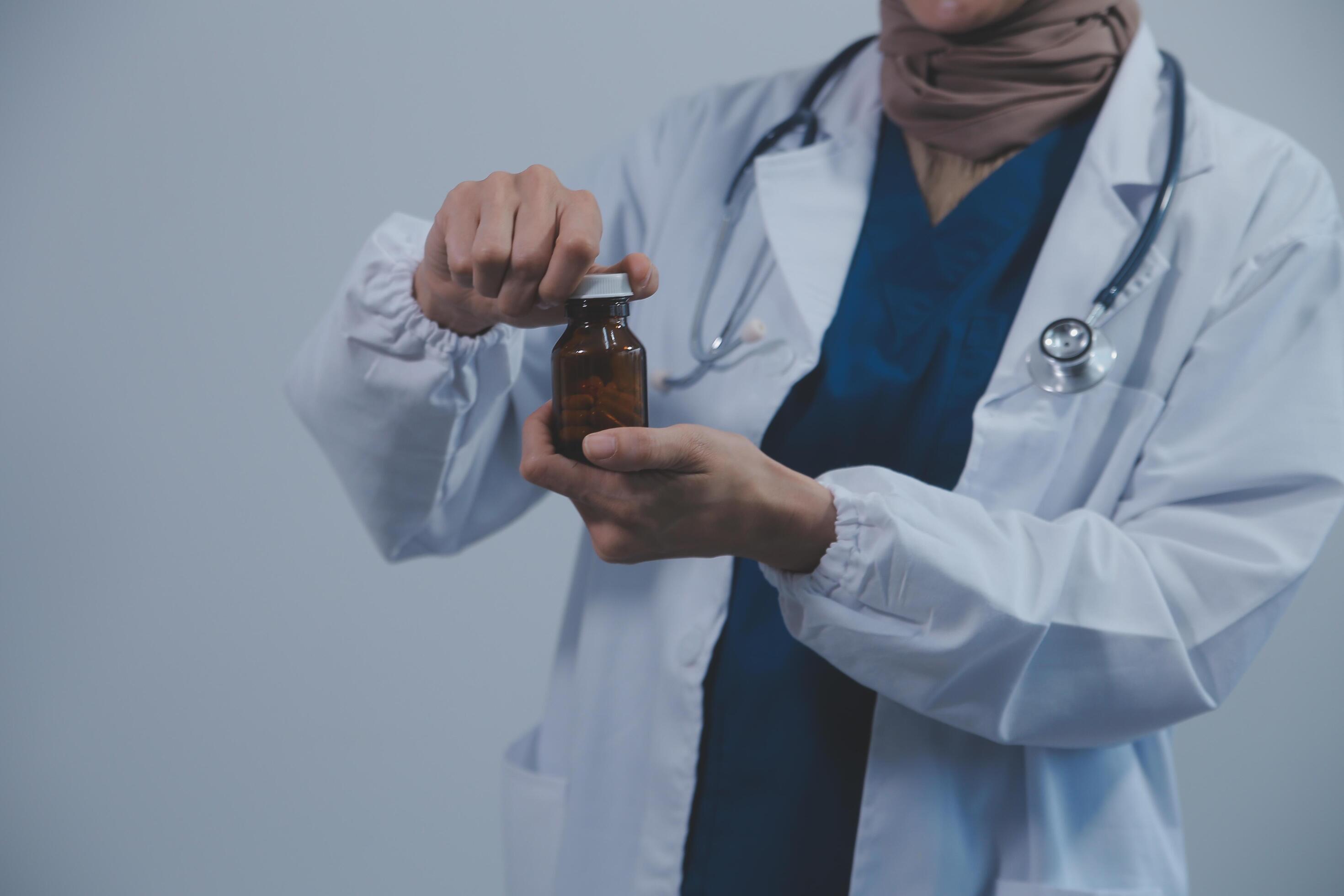 Southeast Asian medical doctor holding a bottle of pills, smiling isolated white background Stock Free