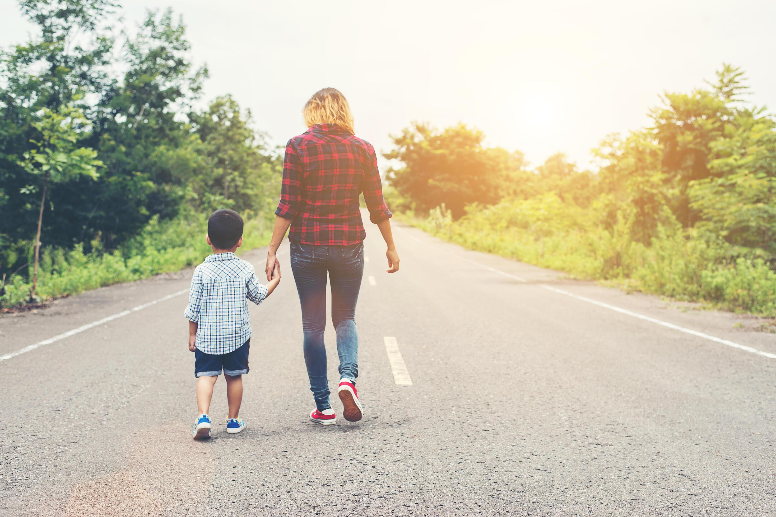 Mother holding a hand of his son in summer day walking on the street. Stock Free