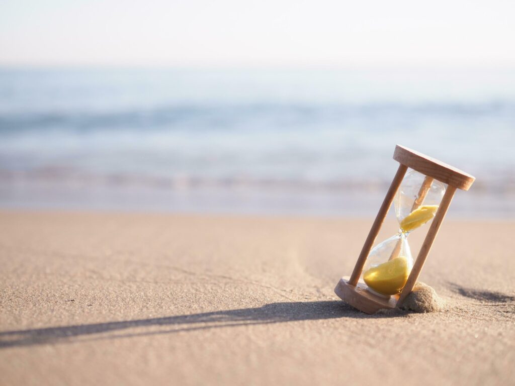 Hourglass on the beach in the sunset time. The concept about countdown to Summer, Travel, Vacation and Relaxation. Stock Free