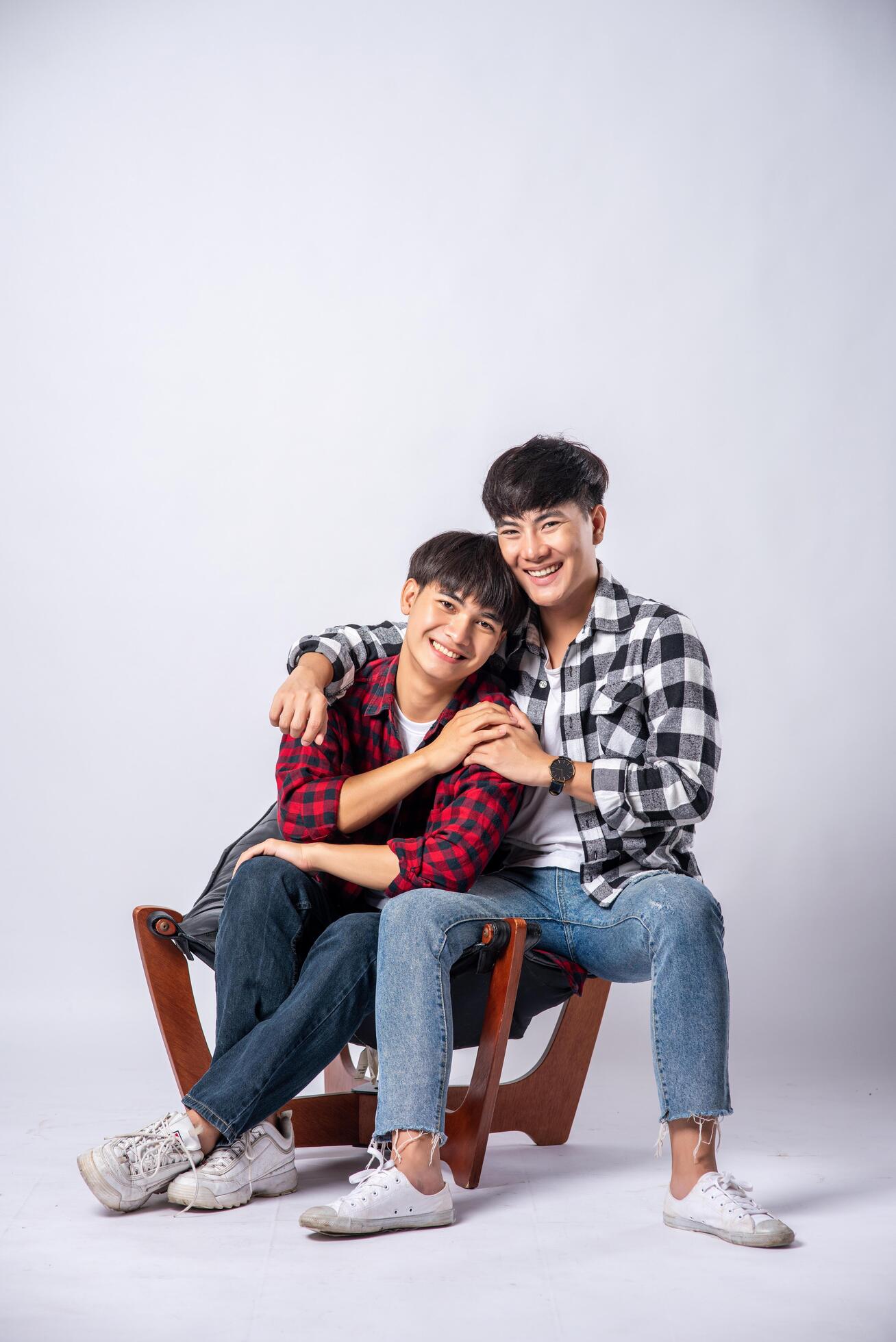 Two men who love each other hug and sit on a chair. Stock Free