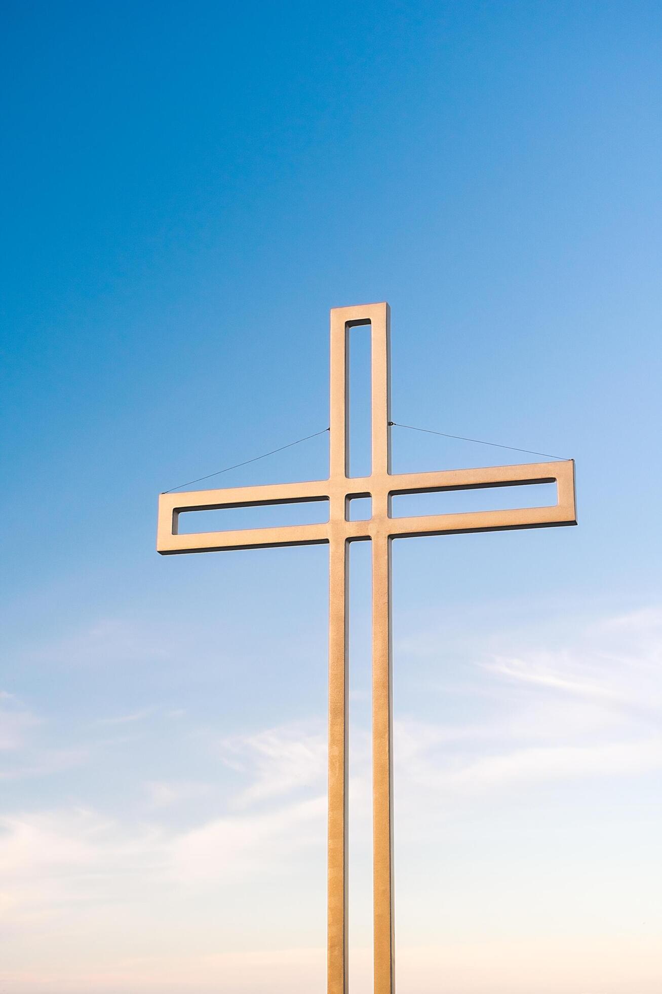 Golden cross against a background of blue sky with clouds. A minimalistic view of a gold-colored cross against the sky. Stock Free