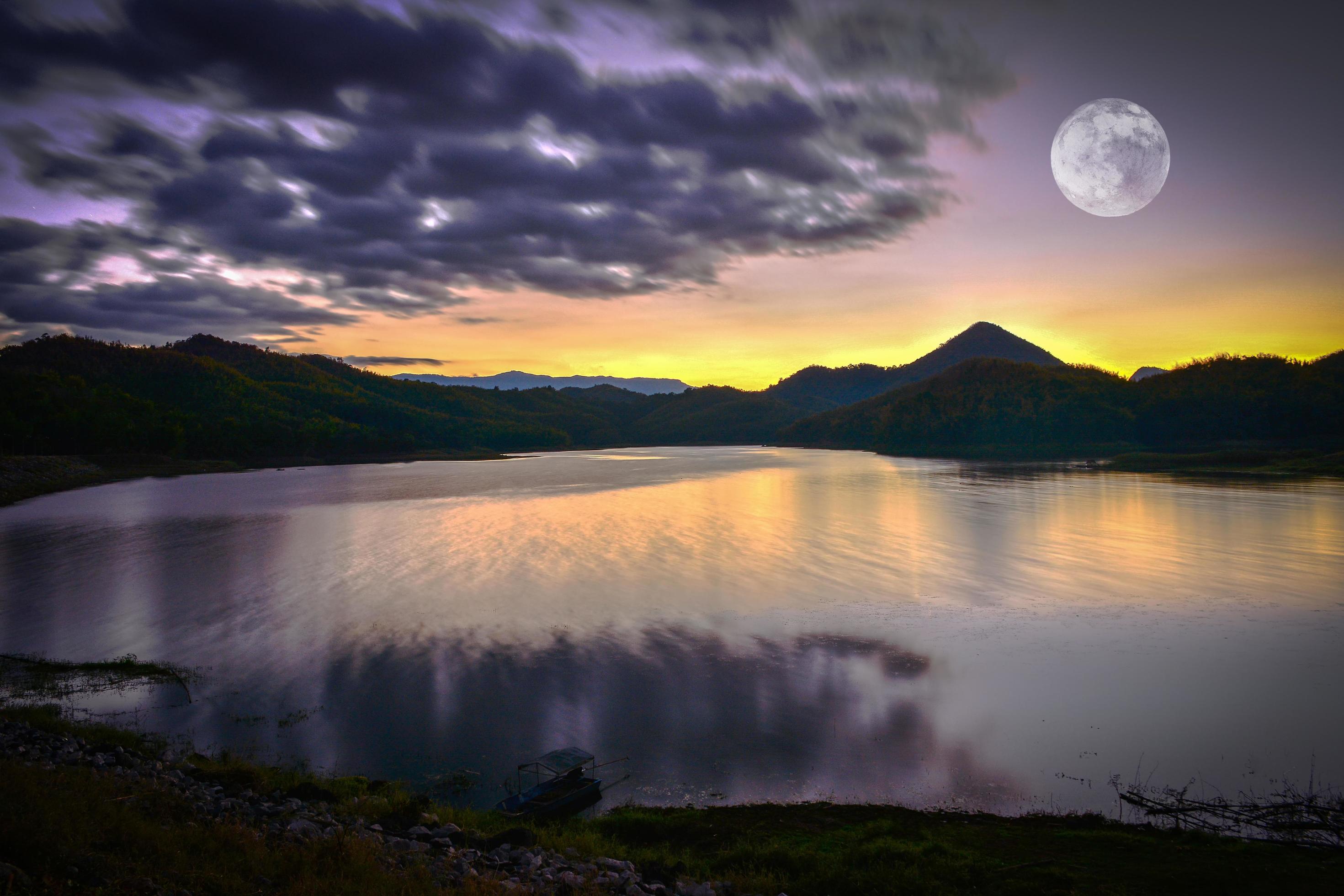 Landscape lake river nature with full moon sunset yellow and purple sky dark clouds moving on silhouette mountain Stock Free