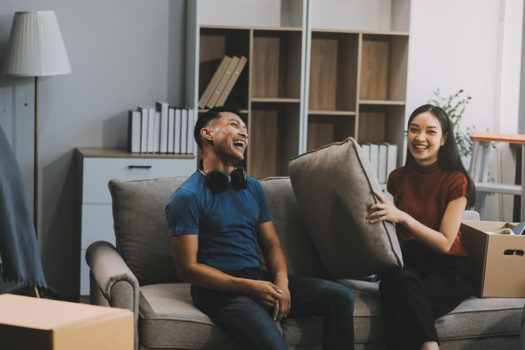 Young happy attractive Asian couple teasing each other with pillow fight on bed. White curtain background. Concept for love and happy relationship. Stock Free