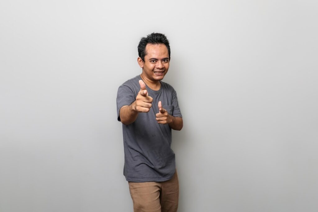 a happy asian man in gray is pointing towards the front isolated on white background Stock Free