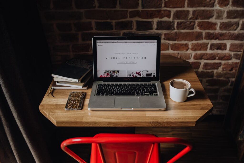 Creatives desk with laptop, camera, journals and books in front of brick wall Stock Free