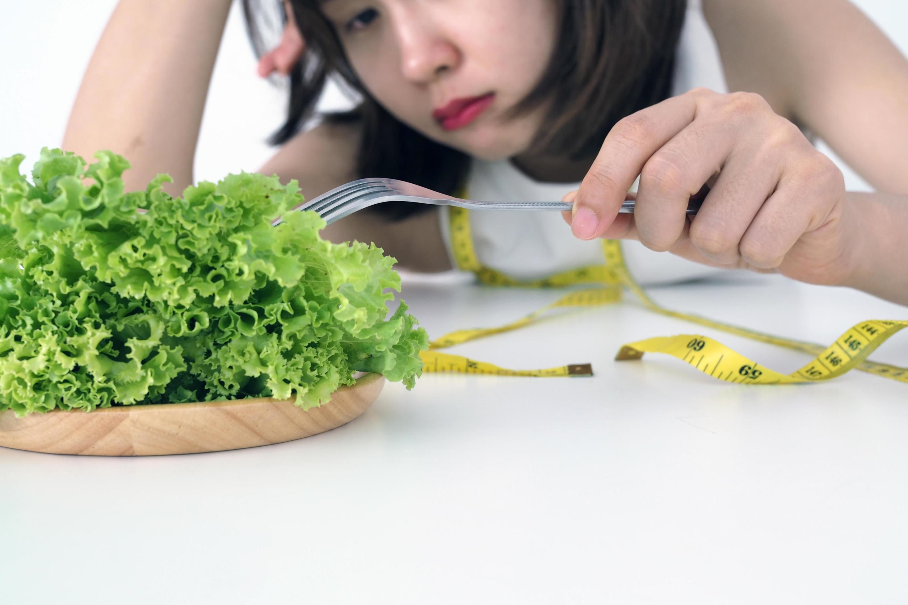 Asian women are tired of eating vegetables using a fork of lettuce in the dish. Healthy Food and diet concept Stock Free