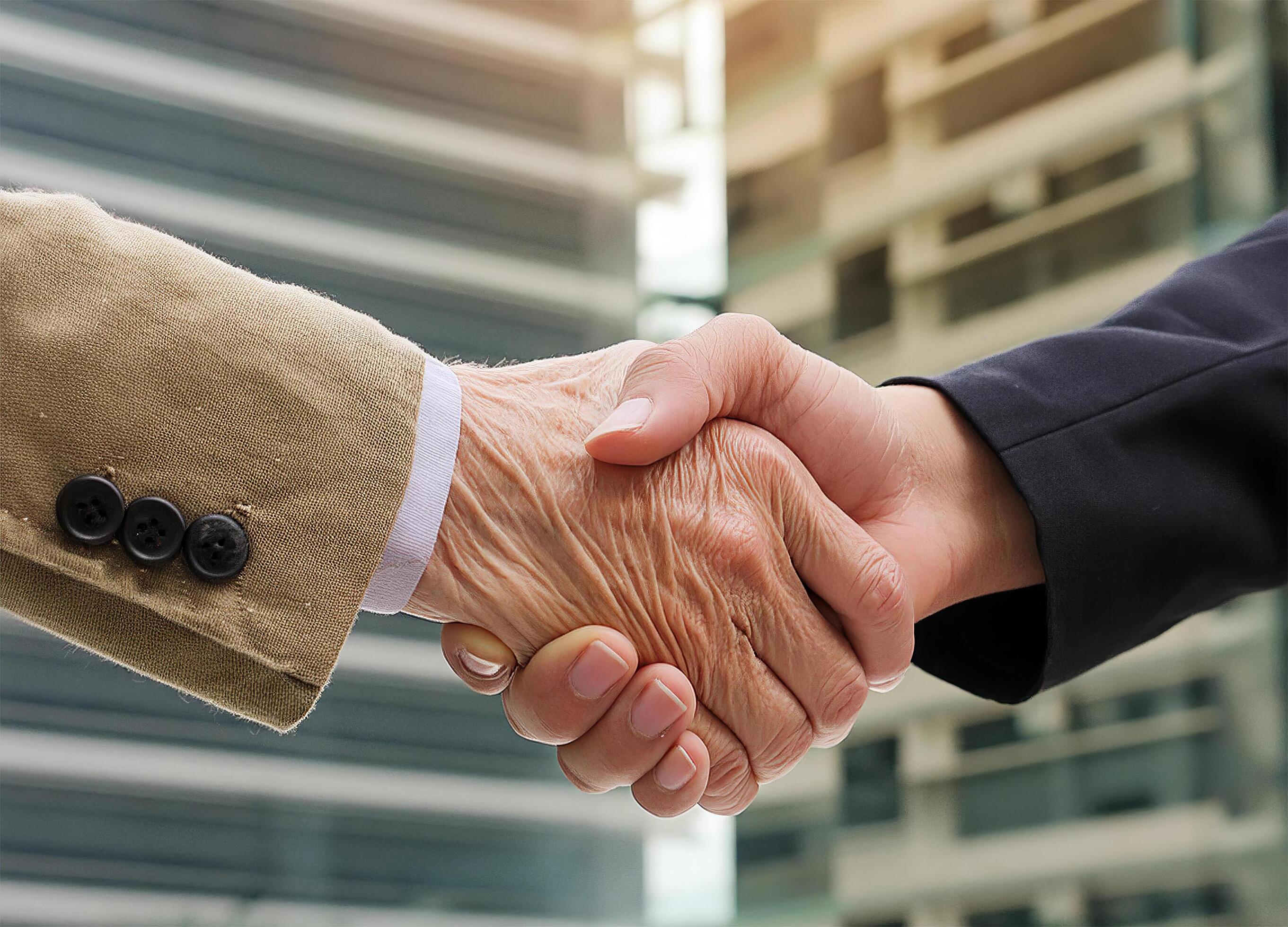 Close up of hand of Two business people ,Old man and woman shaking hands ,building background Stock Free