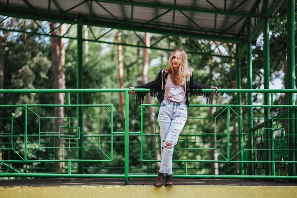 Blonde woman in a black jacket and ripped jeans by a green handrail Stock Free