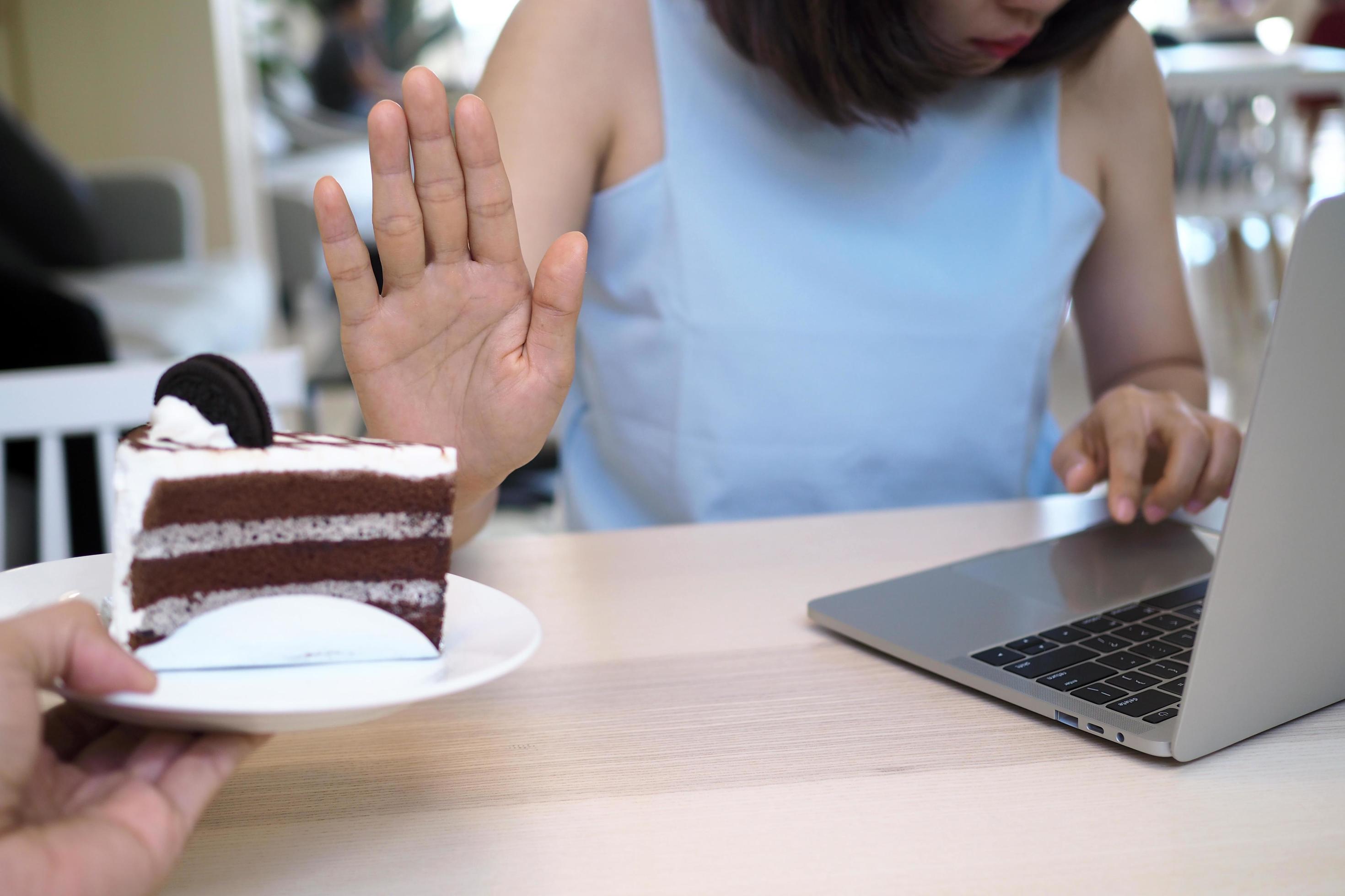 Women refuse to eat cakes while working with computers. Do not eat fussy food during the day for good weight loss. Stock Free