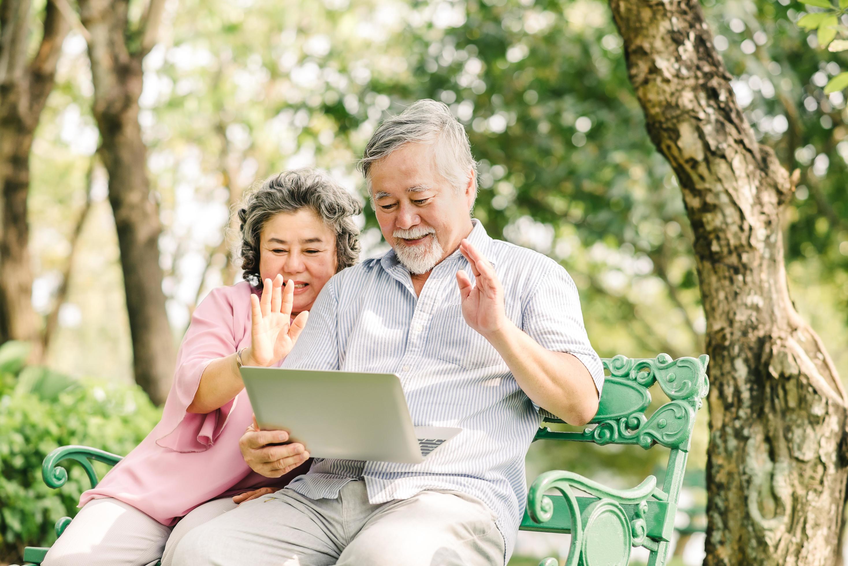 Happy senior Asian couple using laptop outside Stock Free