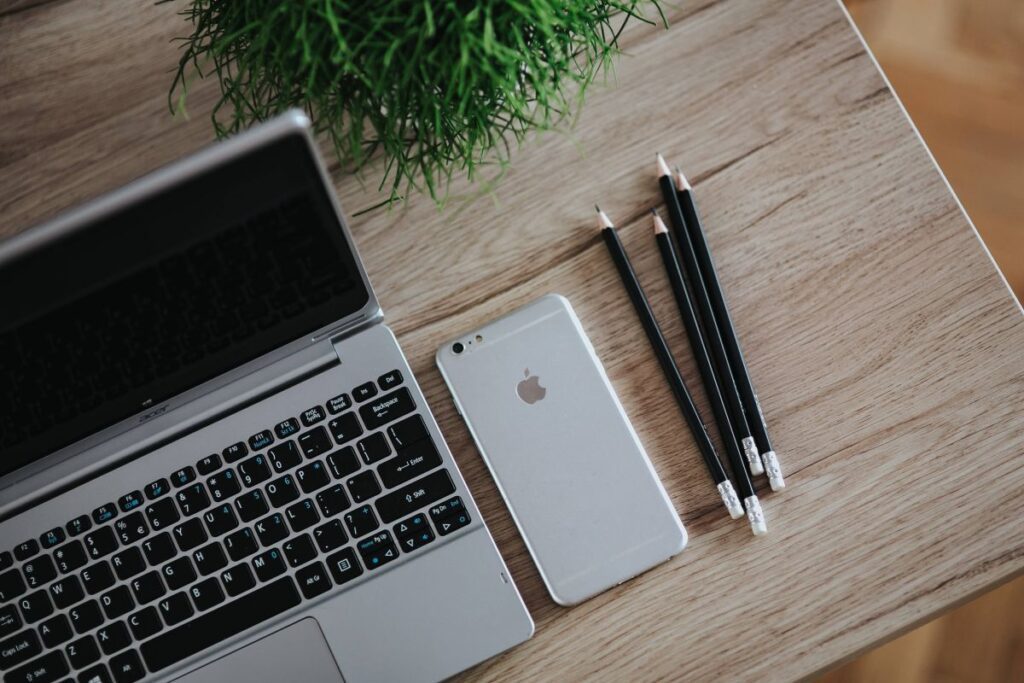 Silver Acer laptop on a wooden desk with a green plant, pencils and an Apple iPhone Stock Free