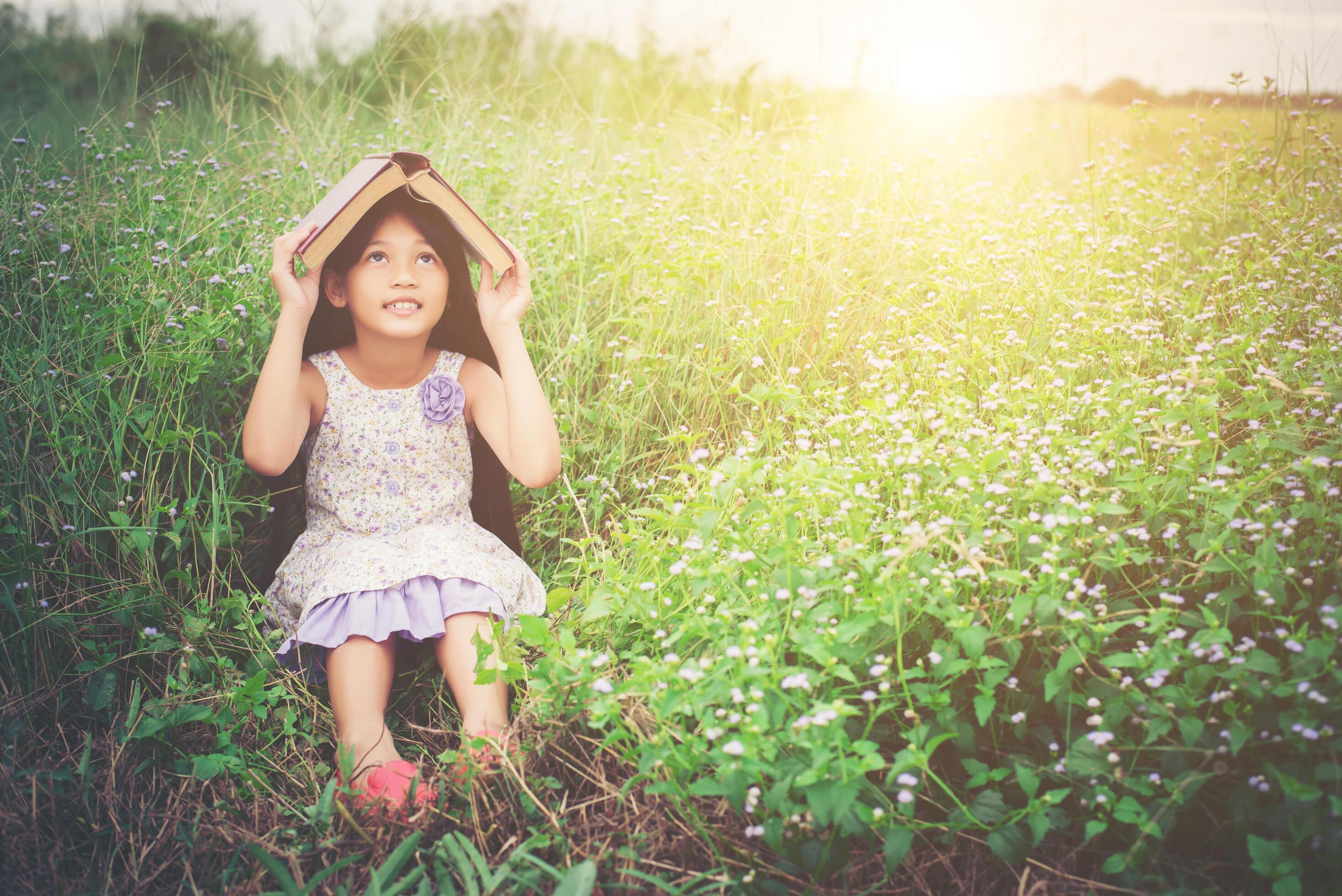 little cute asian girl cover book on her head at nature. Stock Free