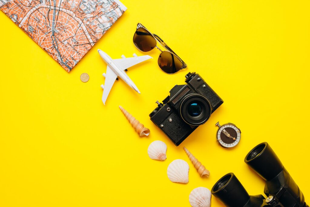 On a yellow background on a diagonal important things are laid out sunglasses, binoculars, the camera, the map Stock Free