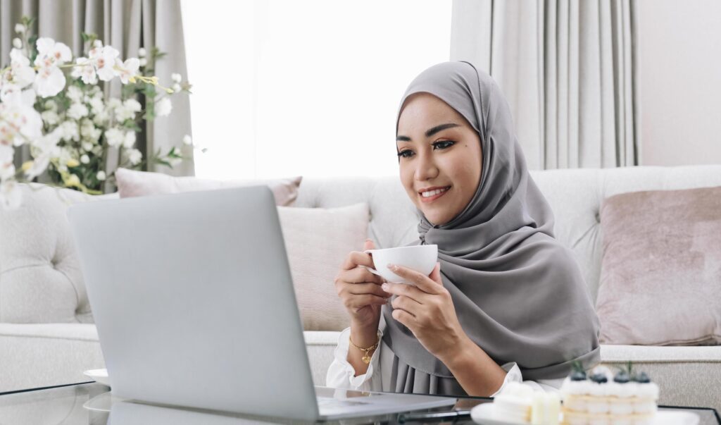 Domestic Lifestyle. Happy Muslim Woman Using Laptop At Home, Watching Movie And Drinking Coffee, Relaxing On Couch In Living Room, Side View Stock Free