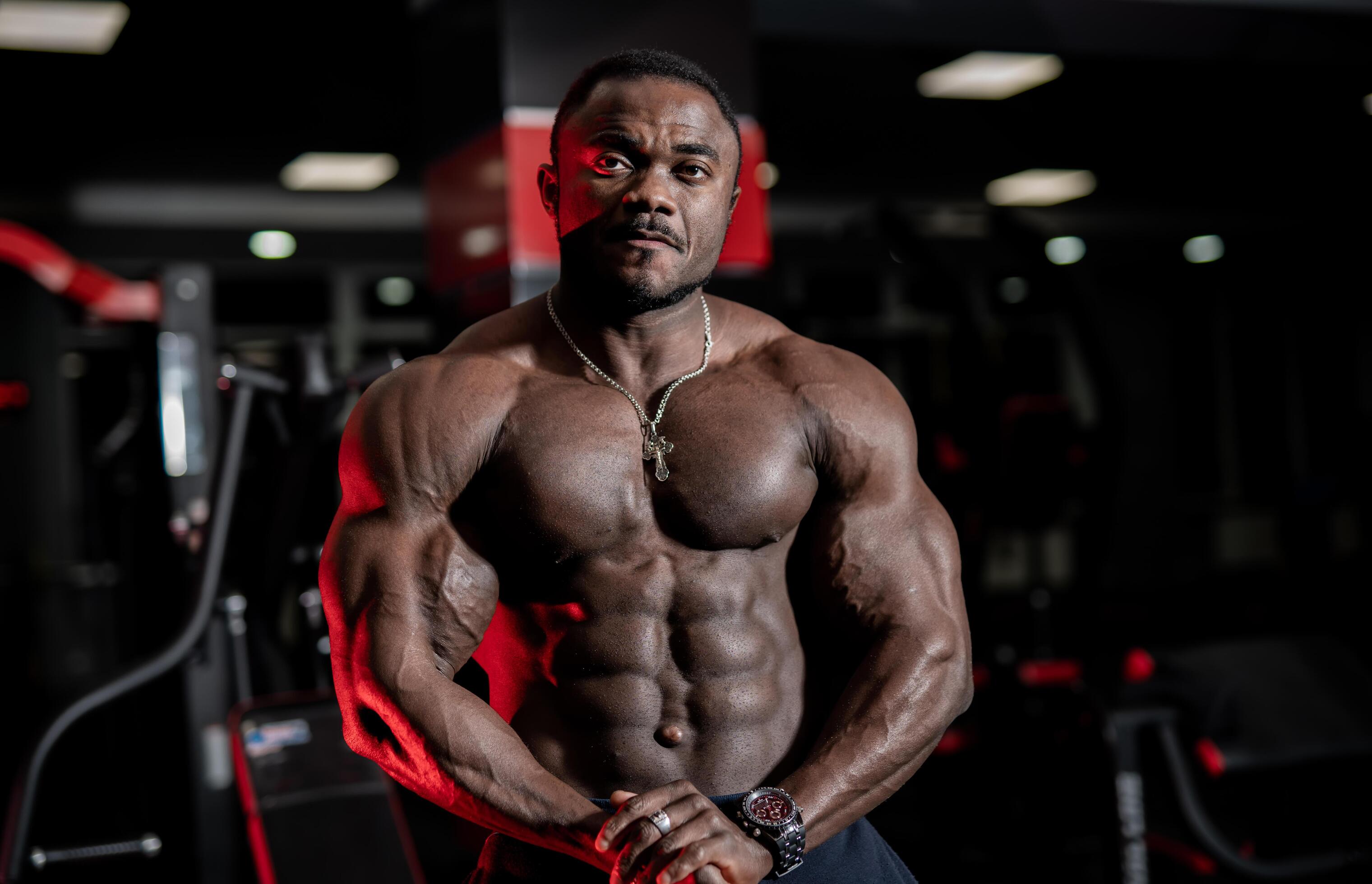 Strong handsome fitness trainer poses with modern sport gym interior on background. Naked torso with perfect muscles. Closeup. Stock Free