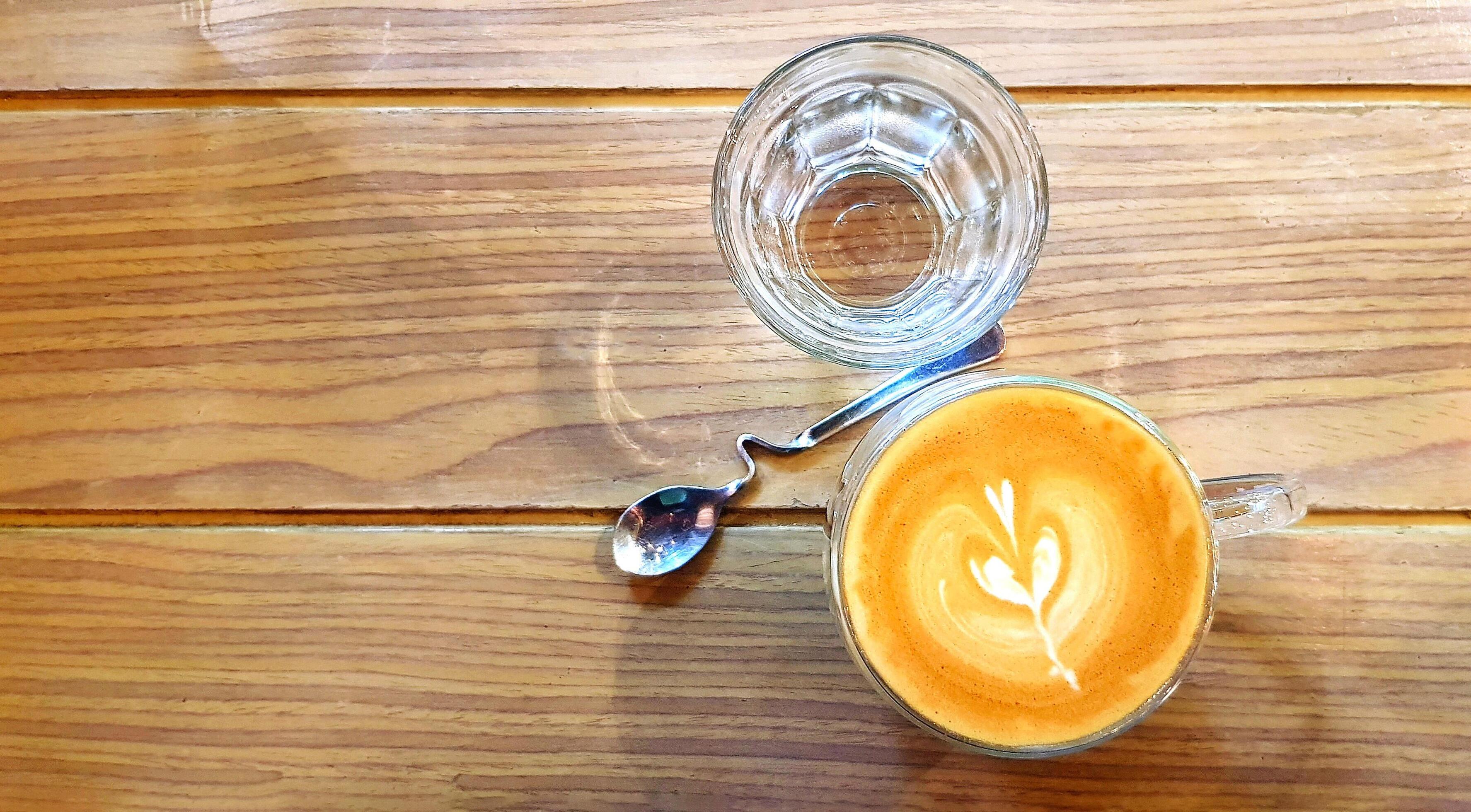 Cup of hot art latte coffee and glass of water with beautiful design spoon on wooden table or wood background with copy space. Stock Free