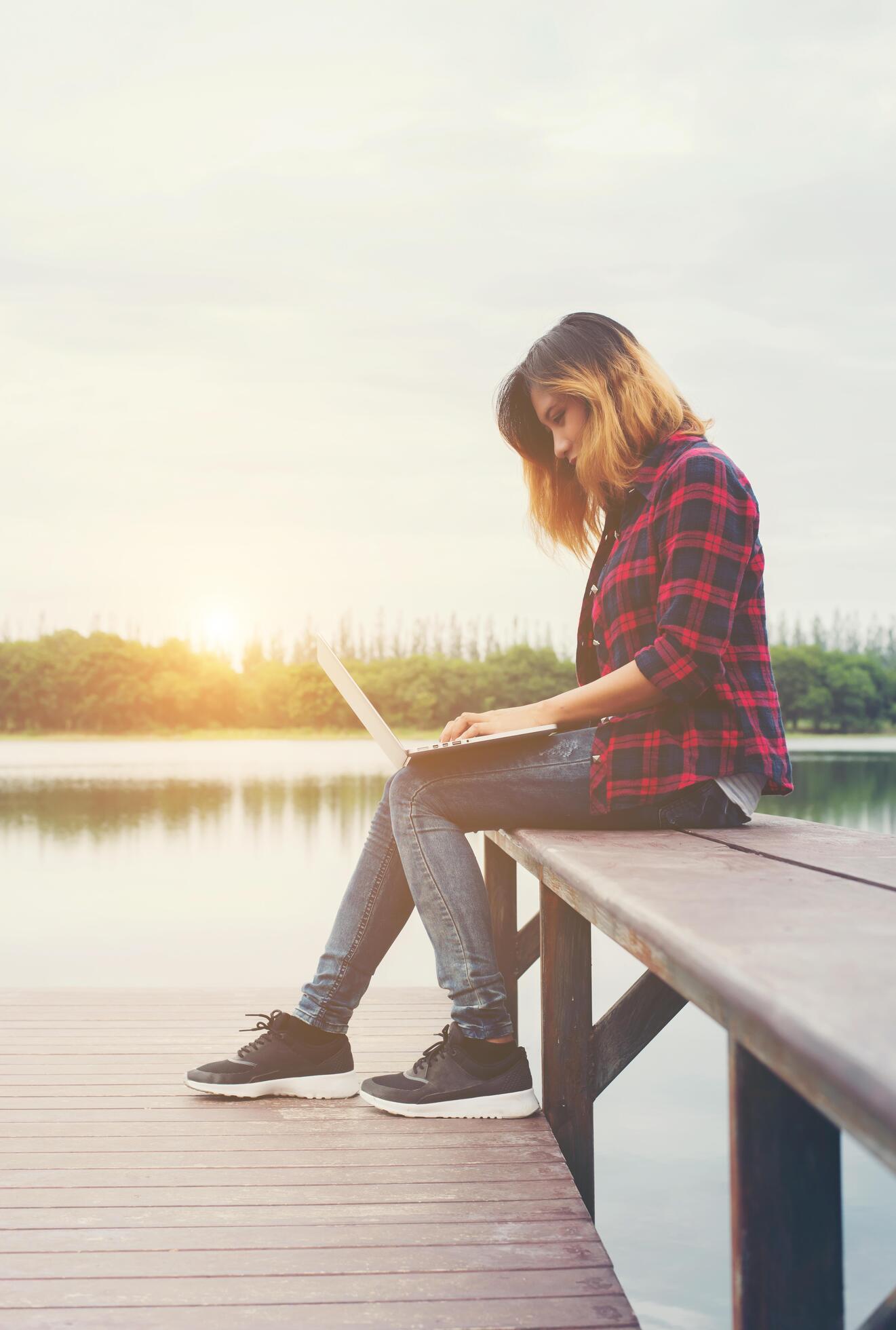 Young happy hipster woman working with her laptop sitting on pier,relaxing enjoy with nature. Stock Free