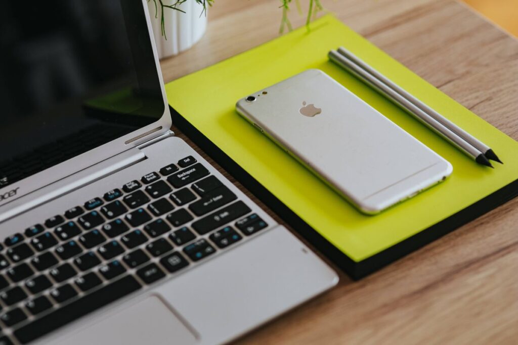 
									Silver Acer laptop, a white Apple iPhone and a notepad on a wooden desk Stock Free