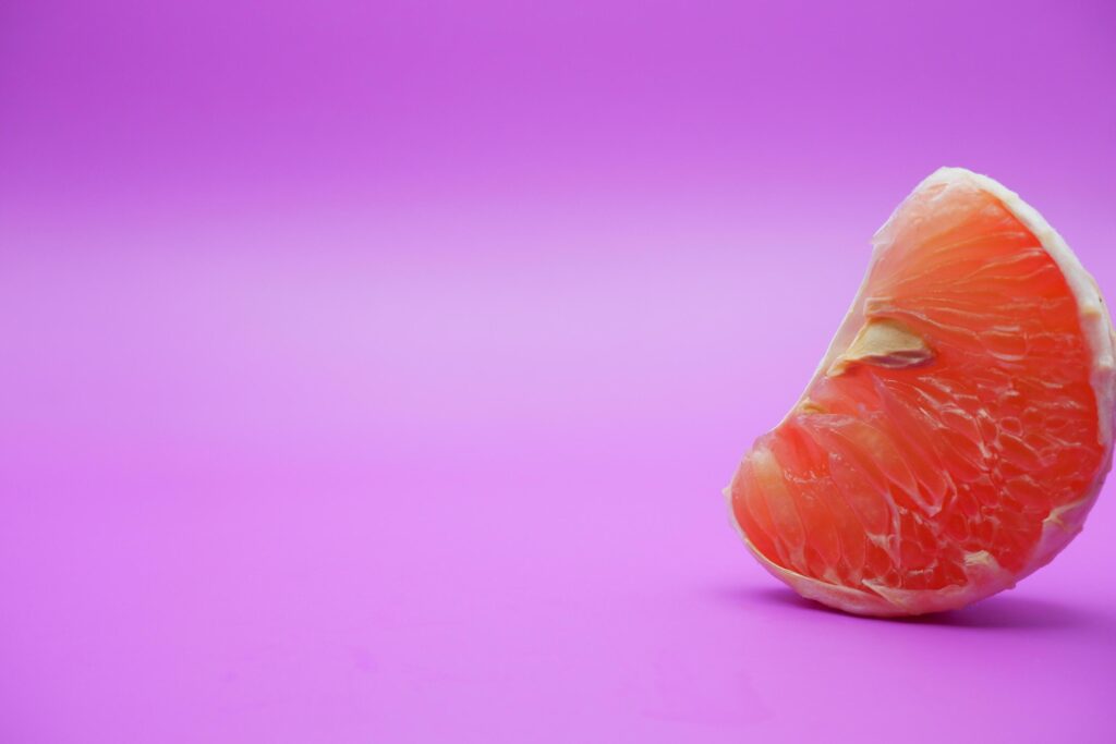 a slice of grapefruit isolated on a purple background. grapefruit that has been peeled until the grain of the orange is visible Stock Free