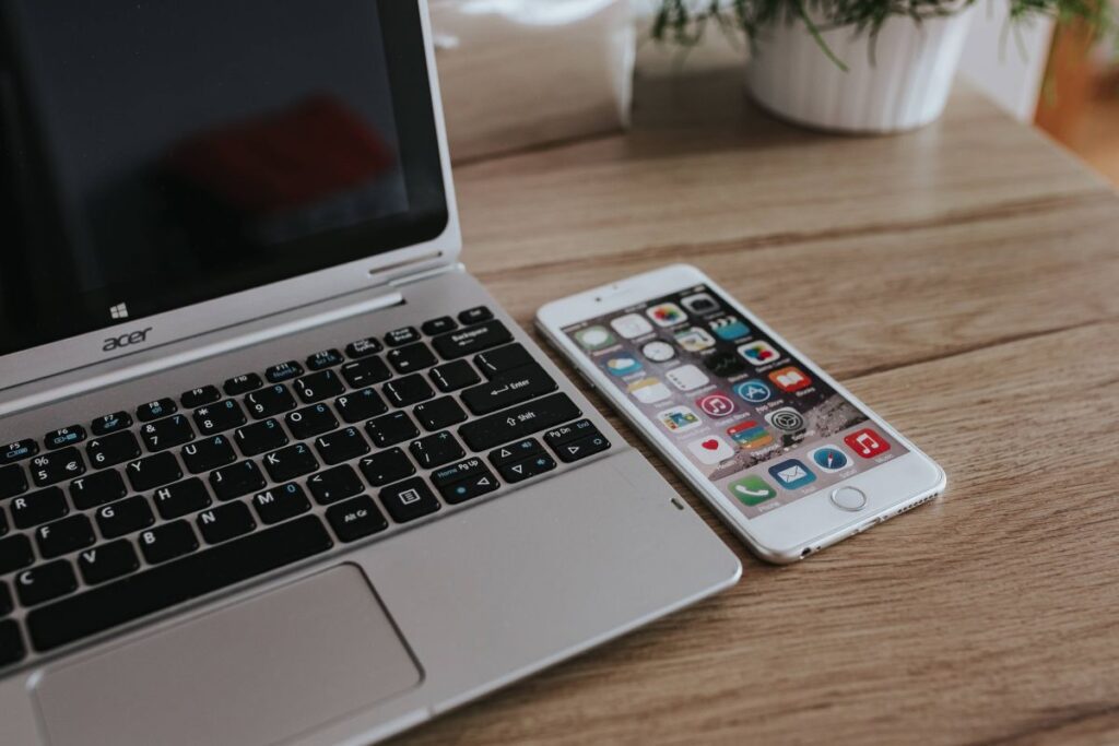 Silver Acer laptop, a white Apple iPhone and a notepad on a wooden desk Stock Free