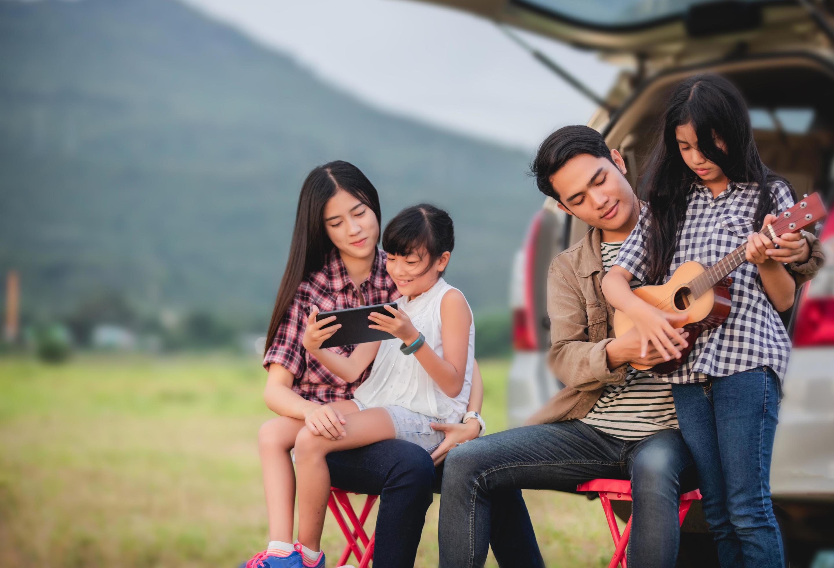 happy little girl playing ukulele with asian family sitting in the car for enjoying road trip and summer vacation Stock Free