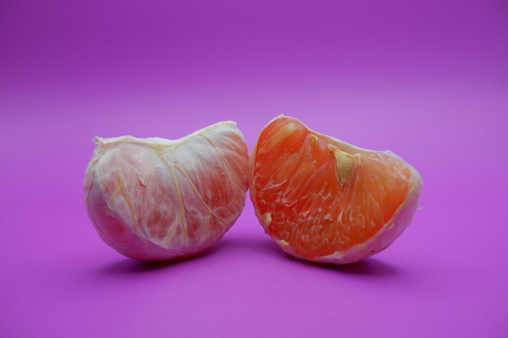 2 grapefruit isolated on purple background. 2 pieces of grapefruit that have been peeled until the grain of the orange is visible Stock Free