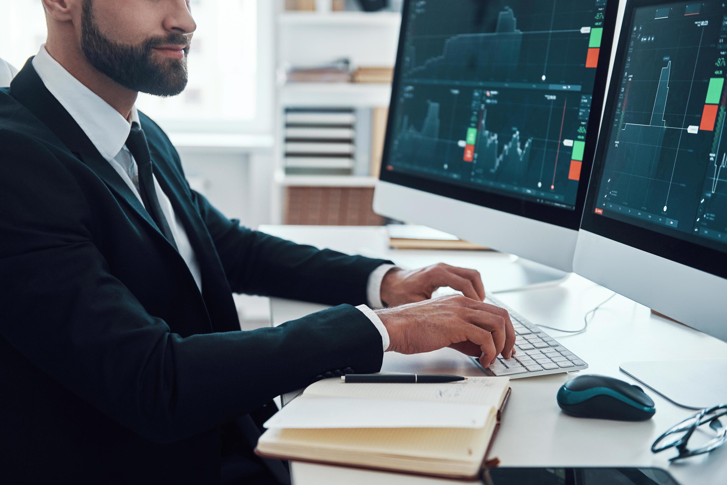 Close up of young man in shirt and tie typing something using computer while working in the office Stock Free