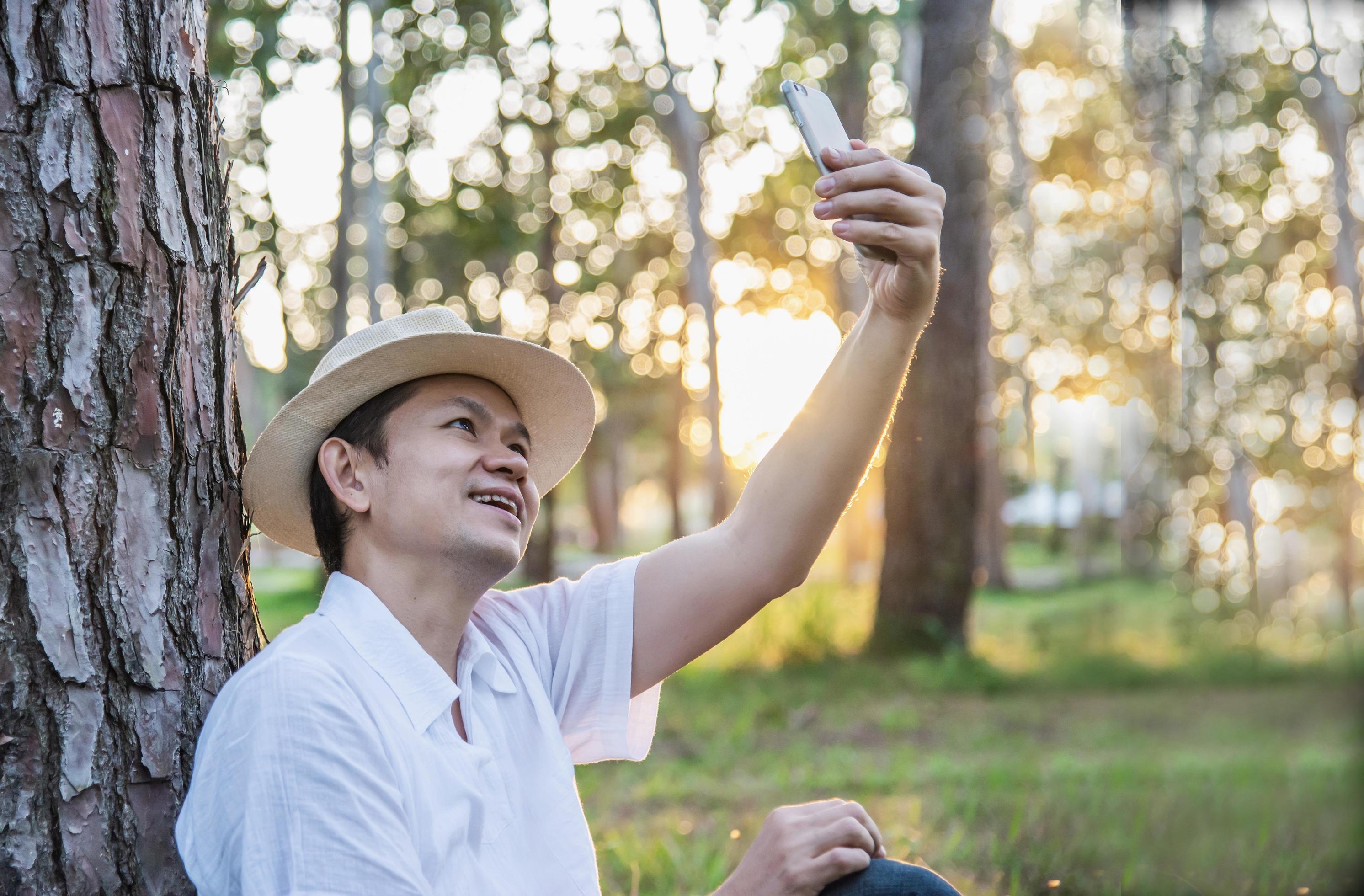 Asian man with mobile phone in forest tree nature – people in spring nature and technology concept Stock Free