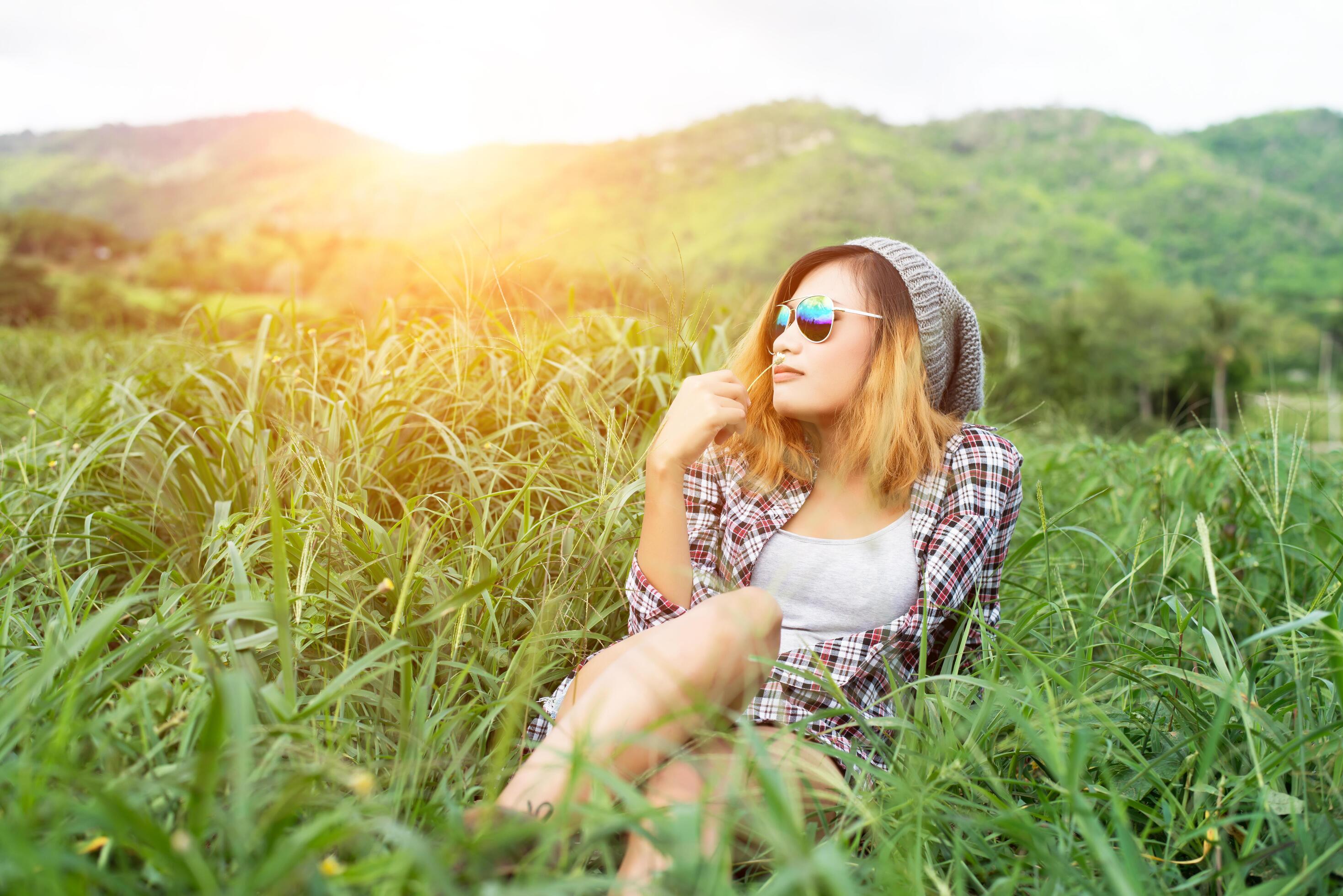 Beautiful hipster woman sitting in a meadow with nature and mountains in the background. Stock Free