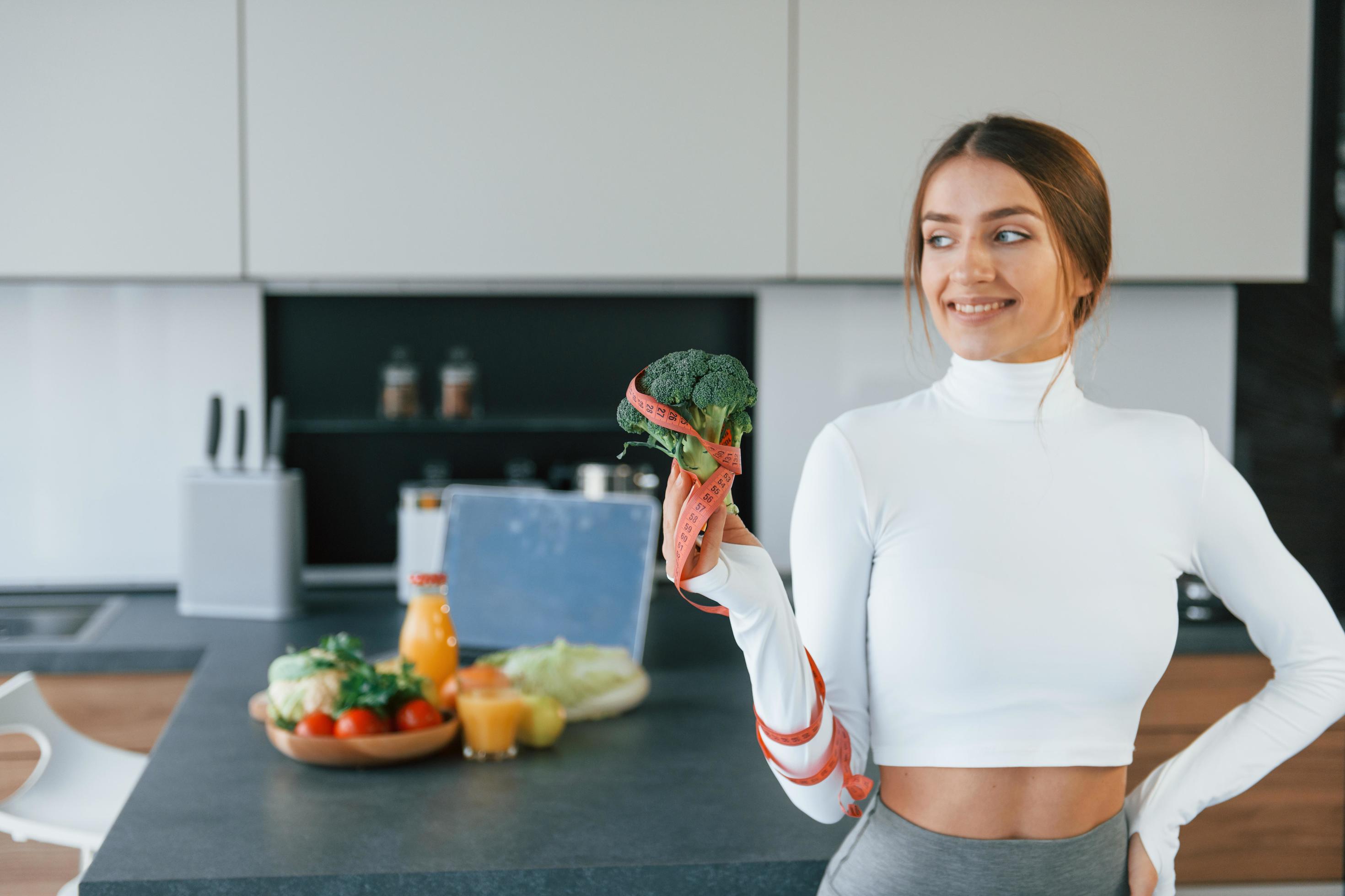 Poses for a camera with vegetables. Young european woman is indoors at kitchen indoors with healthy food Stock Free