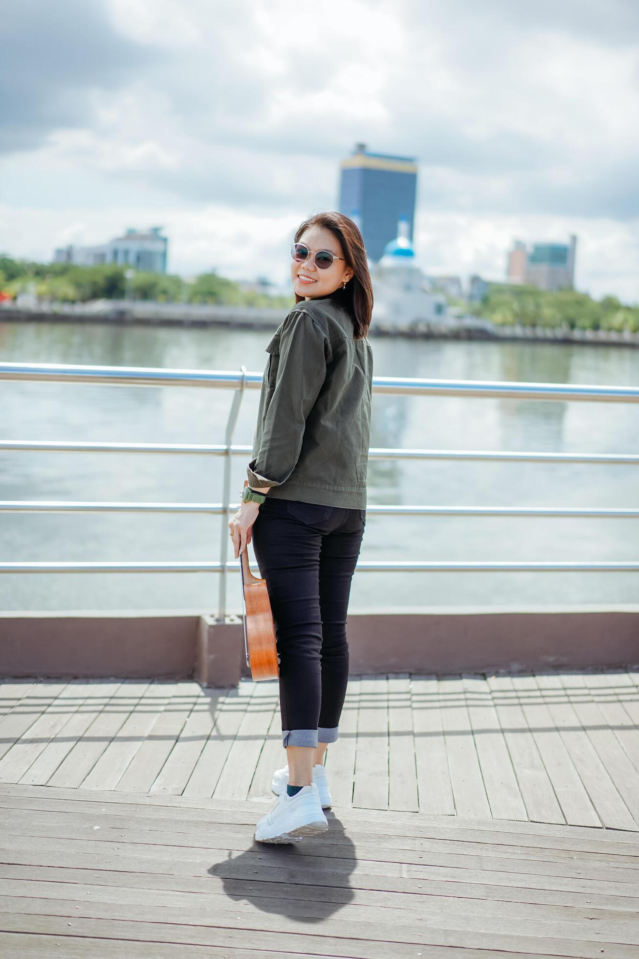 Playing Ukulele of Young Beautiful Asian Woman Wearing Jacket And Black Jeans Posing Outdoors Stock Free