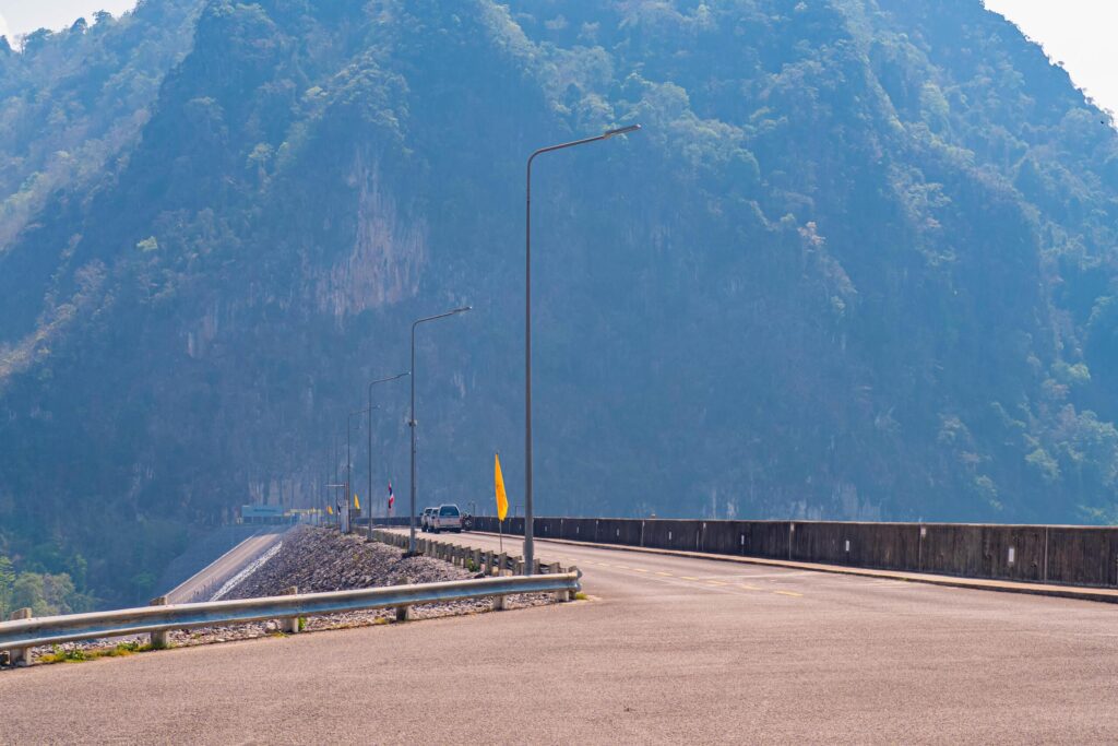 The scene of the road at the top of the dam, with the mountains in the background and a light pole. Stock Free