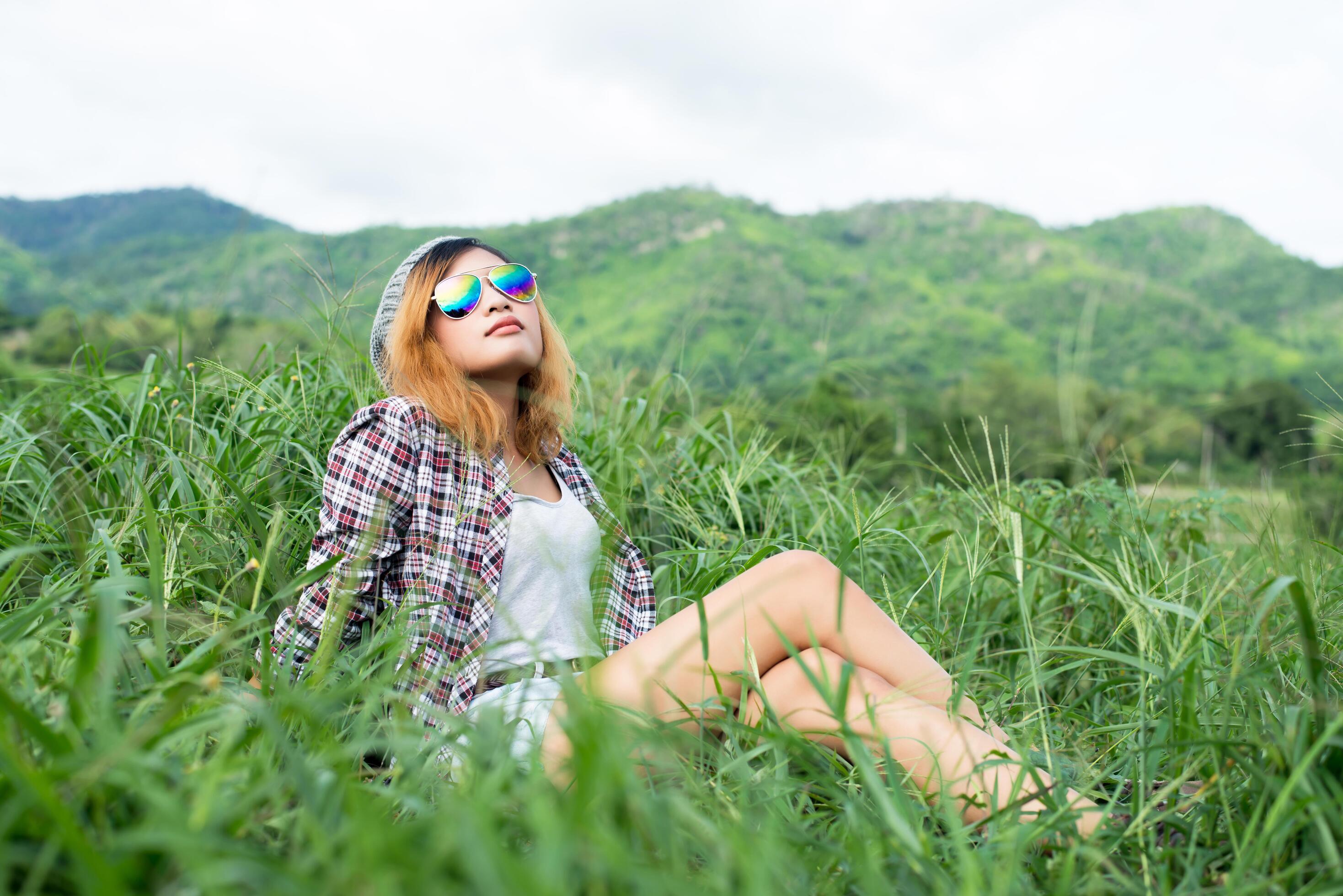 Beautiful hipster woman sitting in a meadow with nature and mountains in the background. Stock Free