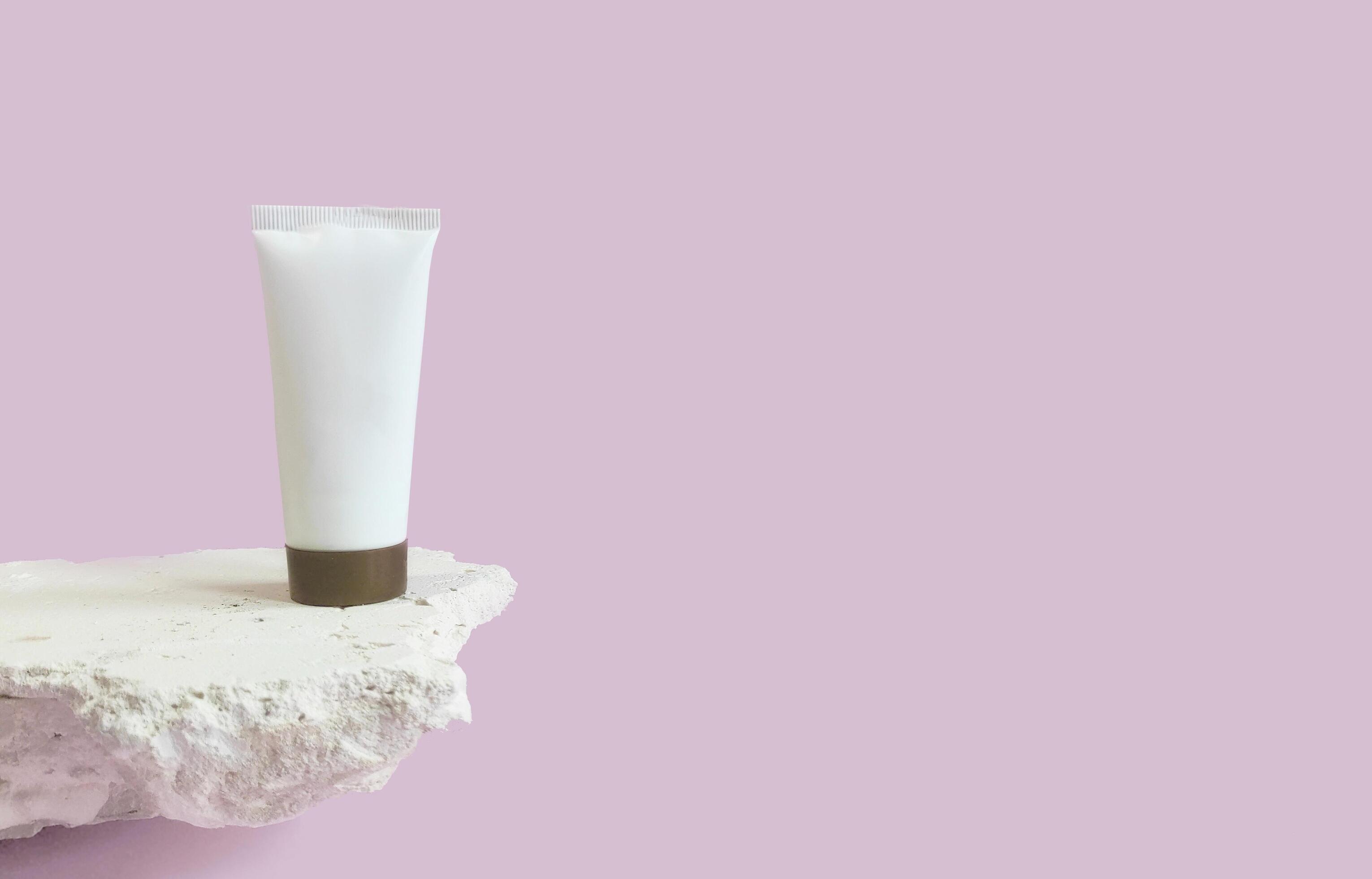 Vertical image with a white empty bottle with a place for a brand of cosmetics on a stone podium on a pink background close-up. Copy space. Stock Free