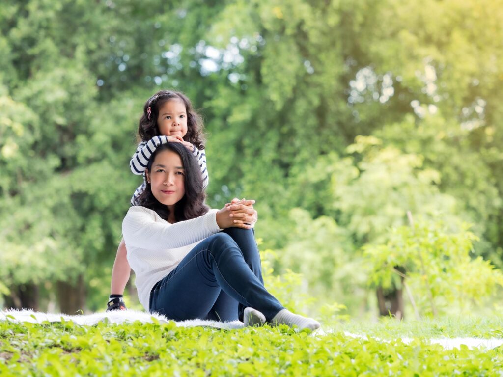 Asian little girl sitting with her mom on the carpet, Relax and learning outside of school to enjoy in the nature park Stock Free