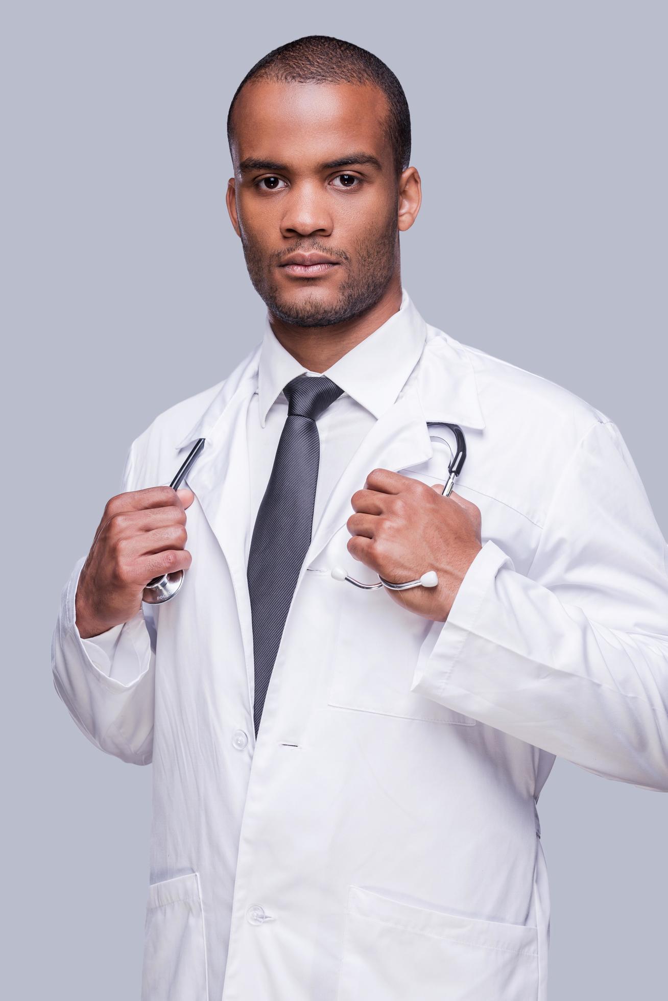 Confident medical expert. Confident African doctor looking at camera and adjusting his stethoscope while standing against grey background Stock Free