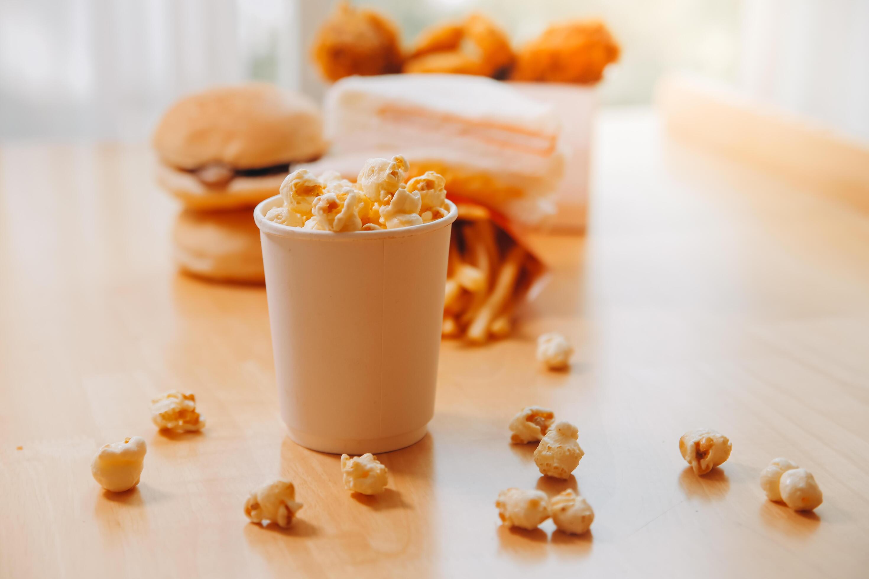 A bucket of popcorn, top-view, warm colors, light brown wooden background, flat lay, daylight macro close-up Stock Free