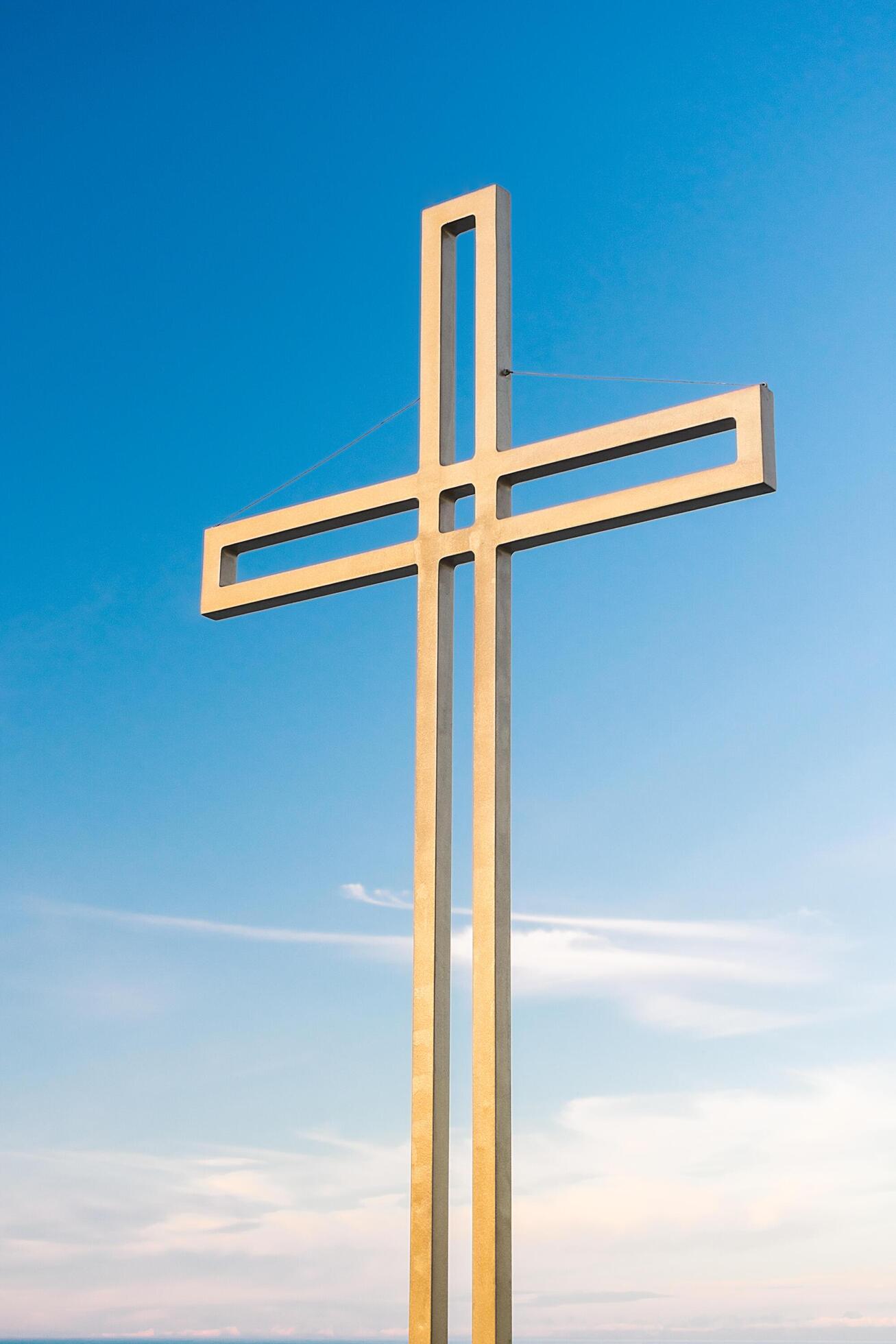 Golden cross against a background of blue sky with clouds. A minimalistic view of a gold-colored cross against the sky. Stock Free