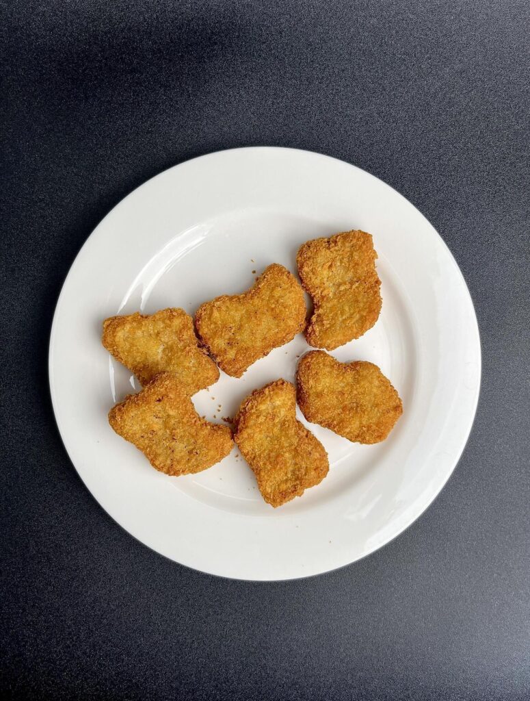 Deep fried crispy and delicious chicken nugget dish on white plate. Food photography isolated on vertical dark black background. Stock Free