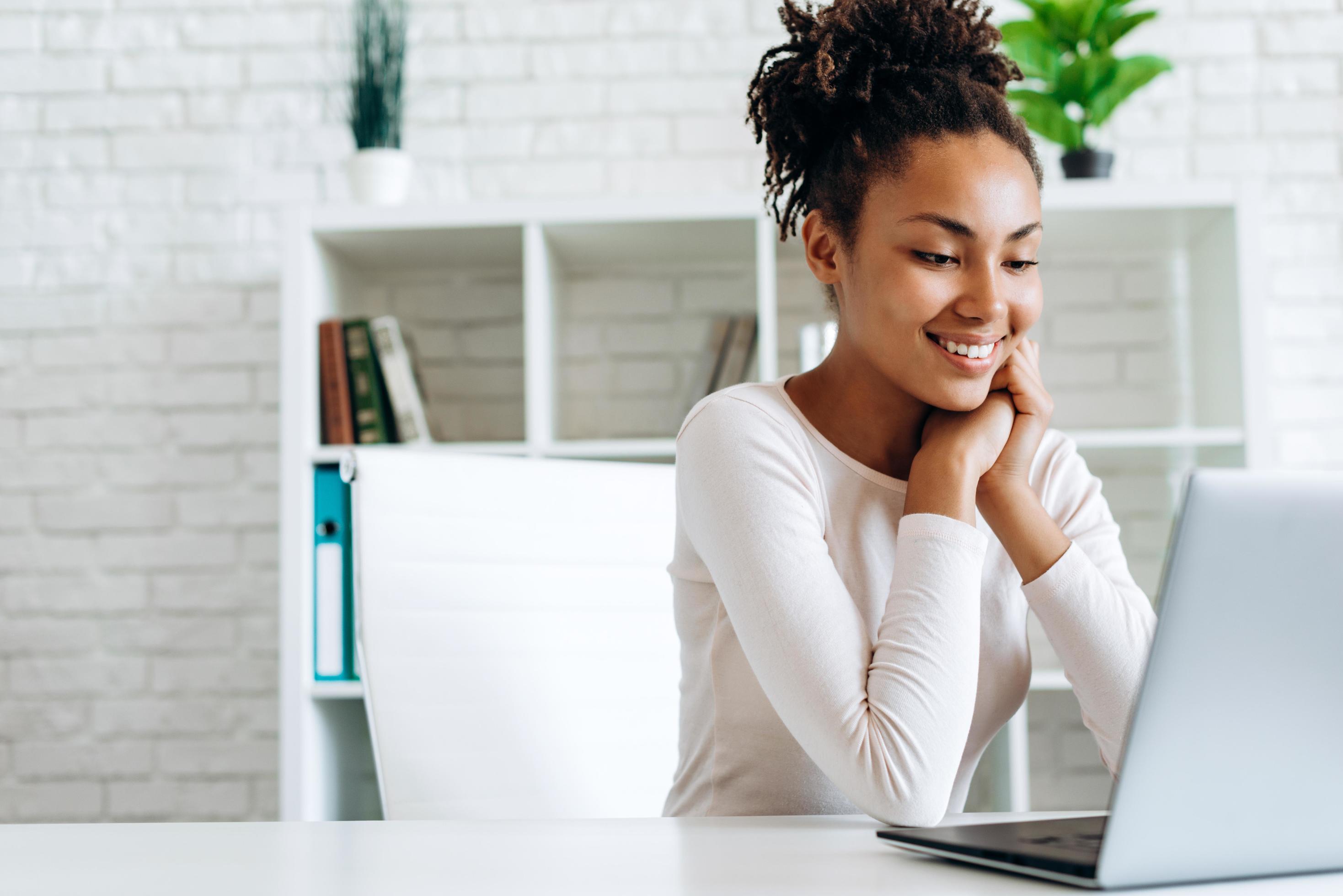 Smiling, attractive girl working at the computer, sitting at the table Stock Free