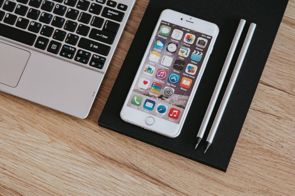 Silver Acer laptop, a white Apple iPhone and a notepad on a wooden desk Stock Free