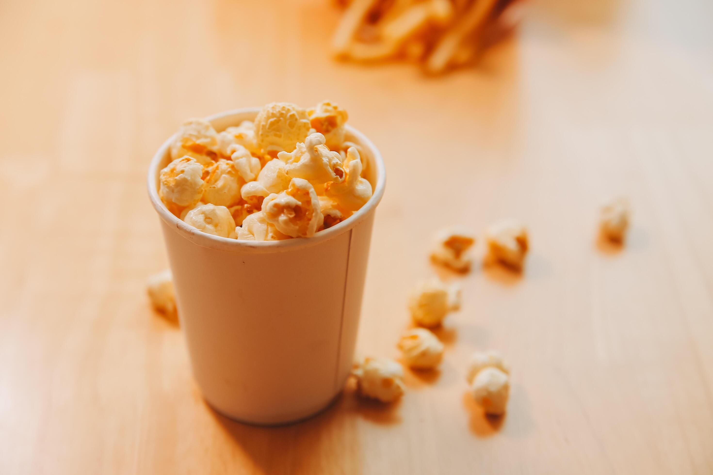 A bucket of popcorn, top-view, warm colors, light brown wooden background, flat lay, daylight macro close-up Stock Free