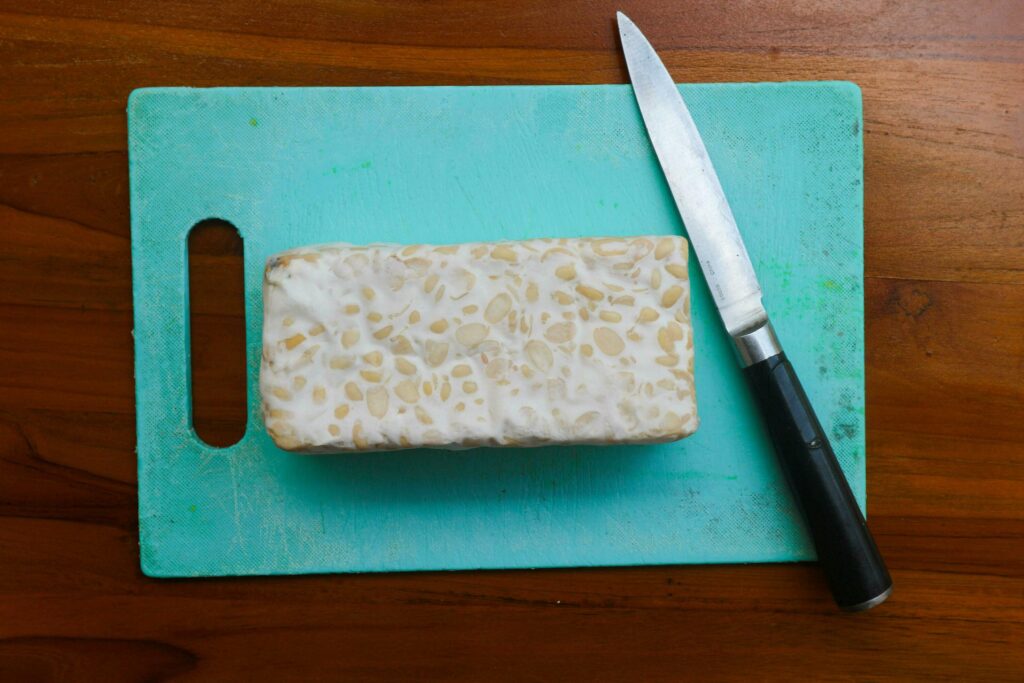 Fresh raw tempeh, on a cutting board and knife for chopping. Food preparation concept Stock Free