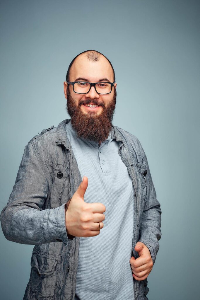 he lifestyle of a successful young man with glasses , beard, fashionable denim jacket showing thumbs up,men’s emotional portrait in Studio Stock Free