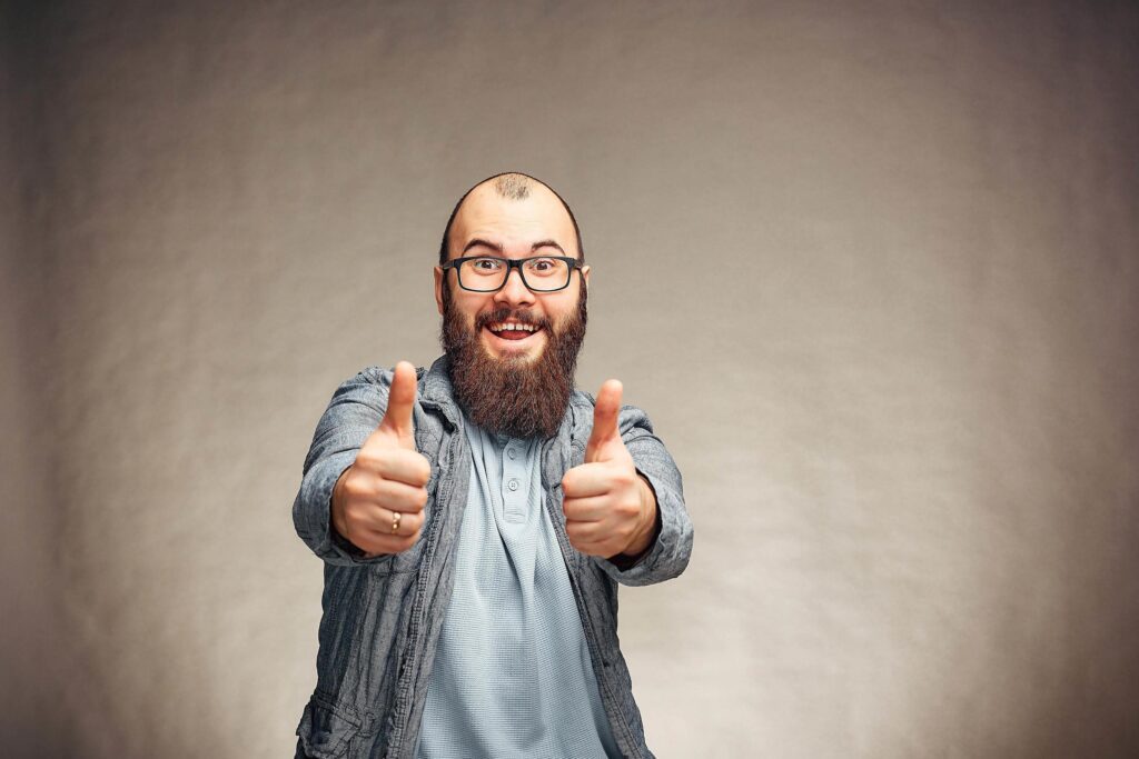 he lifestyle of a successful young man with glasses , beard, fashionable denim jacket showing thumbs up,men’s emotional portrait in Studio on a plain background. Stock Free